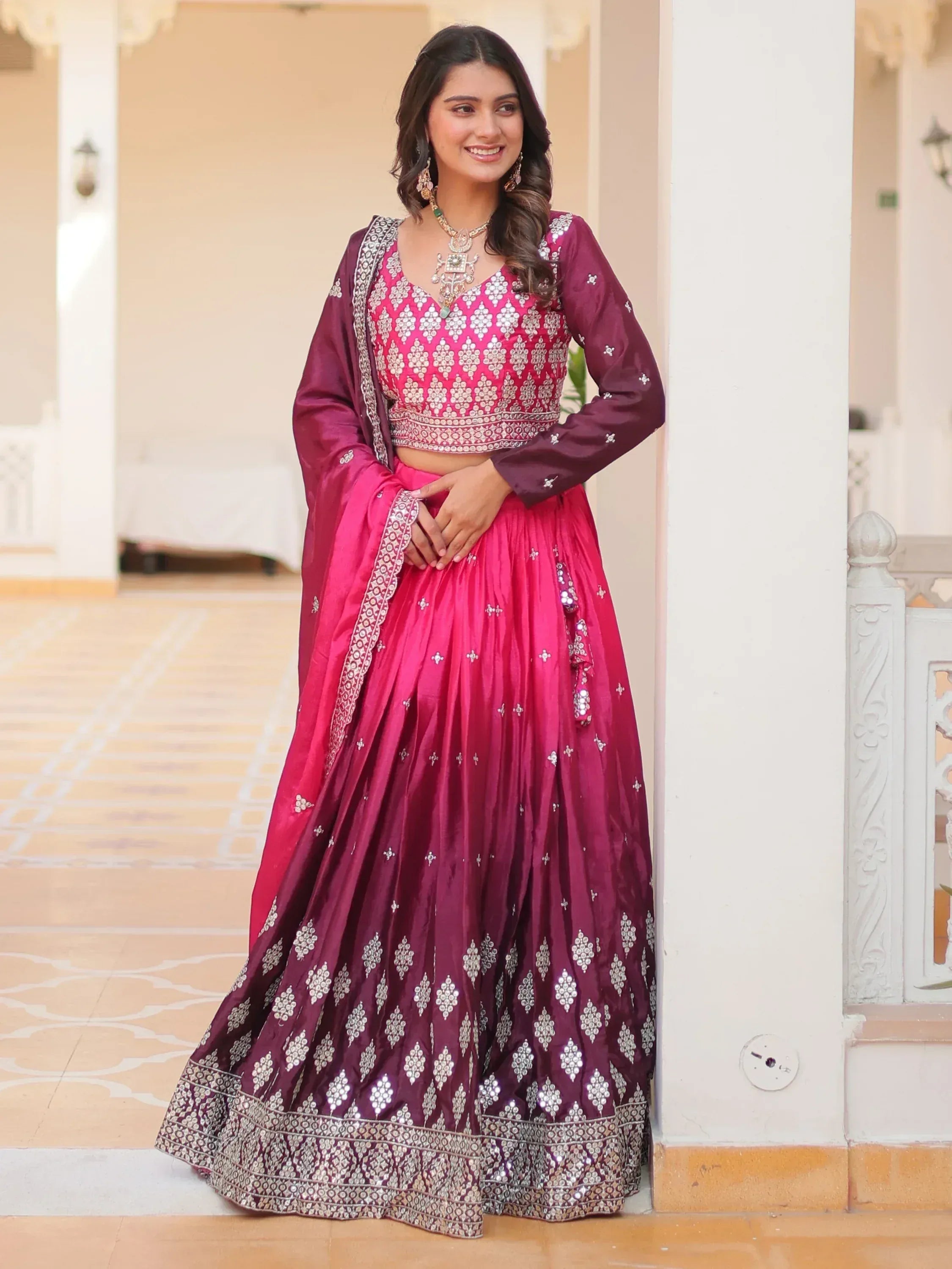 Woman in maroon and pink embroidered lehenga choli with mirror work, perfect for Indian weddings and festive occasions.
