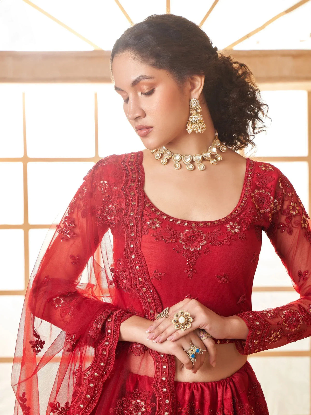 Red embroidered lehenga choli with sheer sleeves, gold jewelry, and floral detailing for Indian ethnic wear