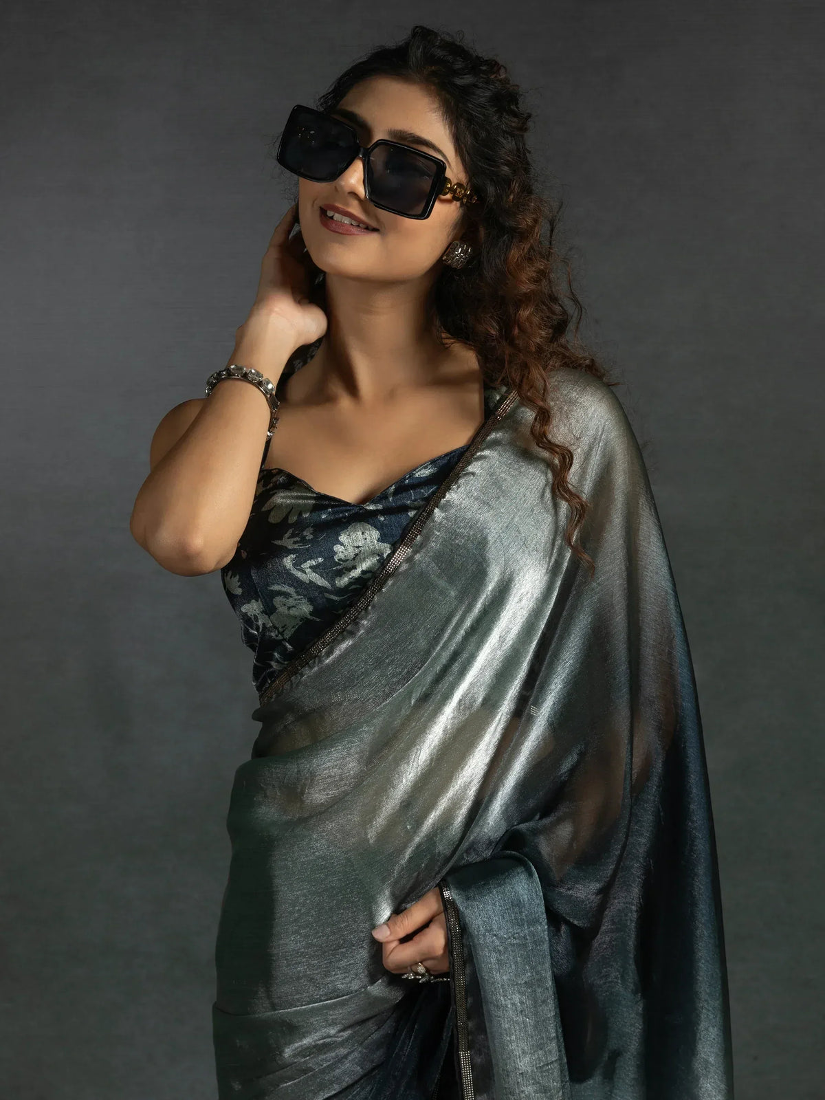 Stylish woman in shimmering silver saree with floral blouse, wearing oversized sunglasses for ethnic fashion look