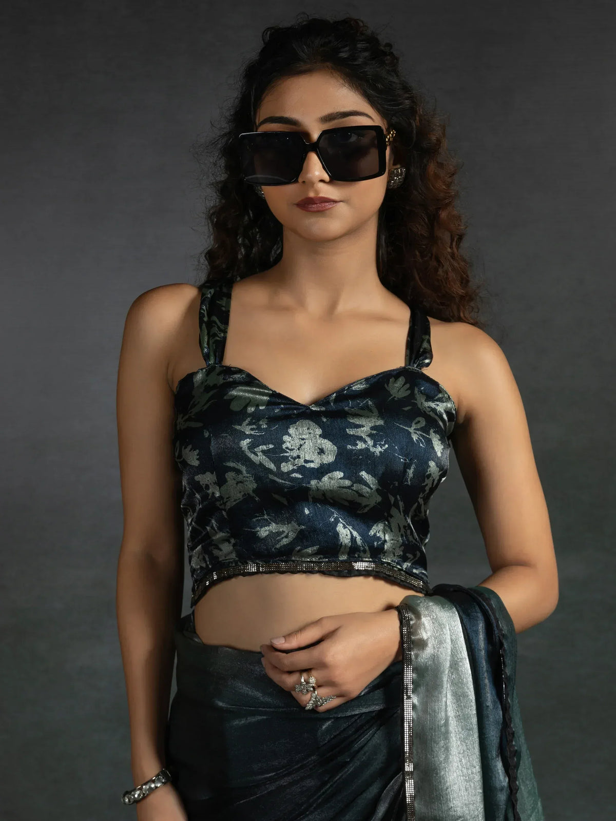 Stylish woman in dark floral velvet blouse with sequin trim, paired with matching saree, wearing oversized sunglasses.