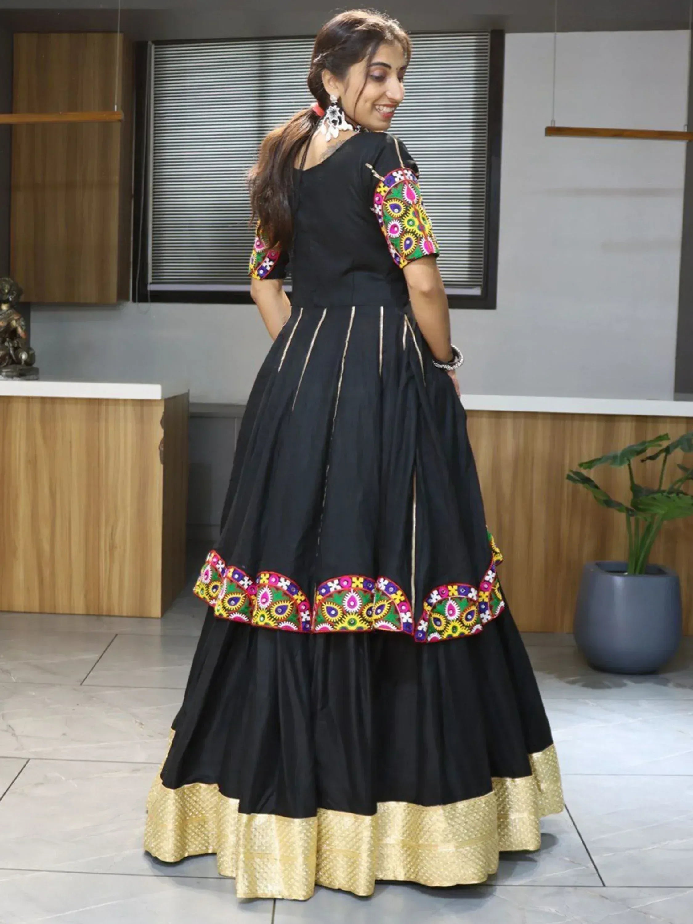 Black ethnic gown with colorful mirror work and gold border, perfect for Indian festive occasions.