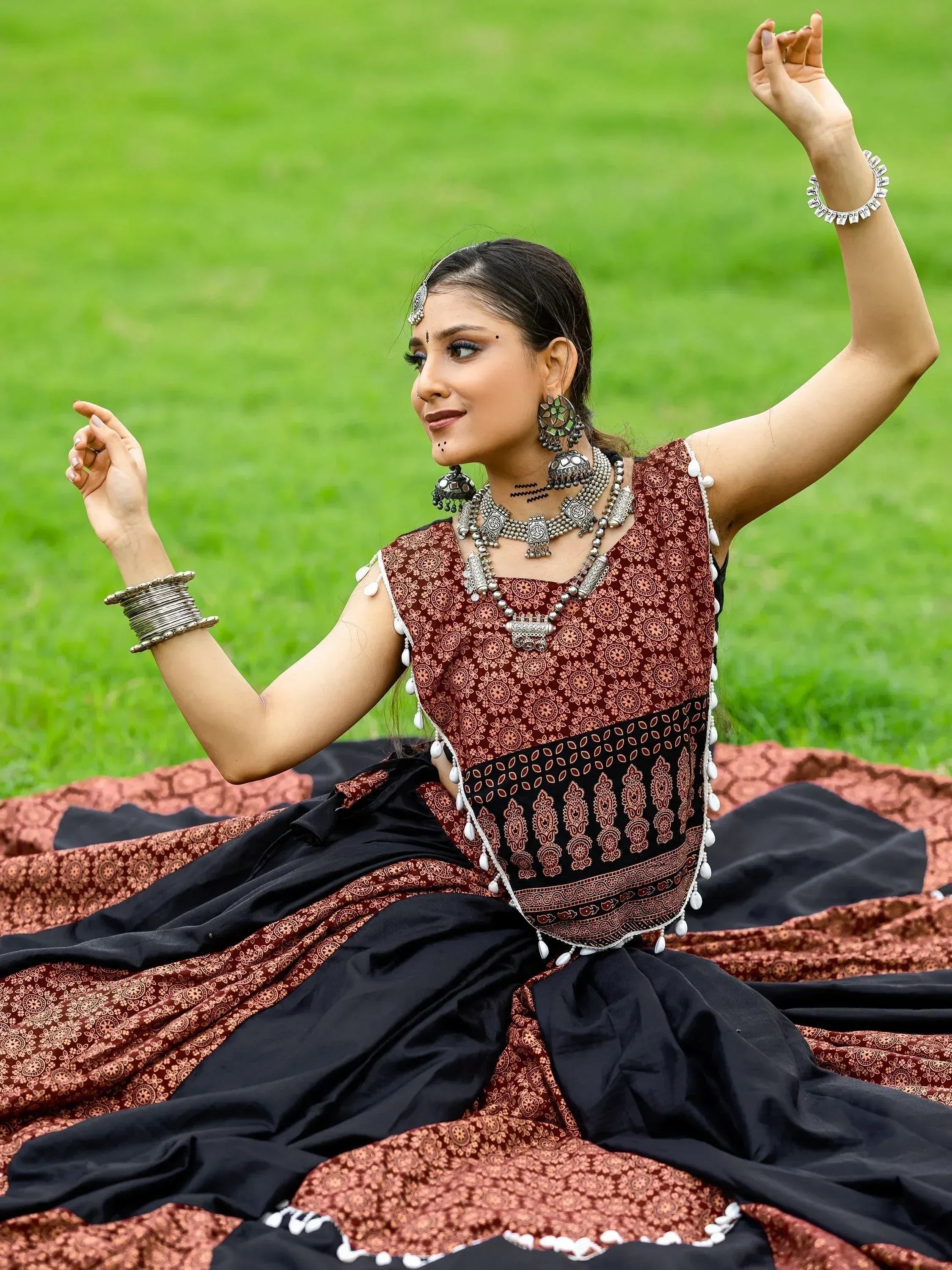 Woman in maroon and black ethnic lehenga with silver jewelry, posing on grass