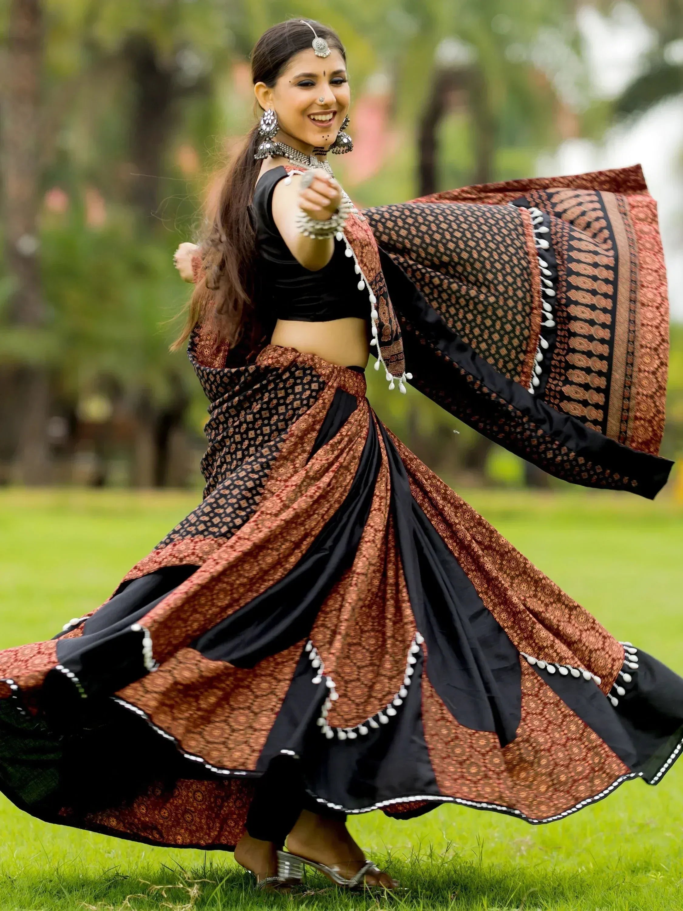 Woman dancing in black and rust Indian ethnic lehenga choli with traditional jewelry outdoors