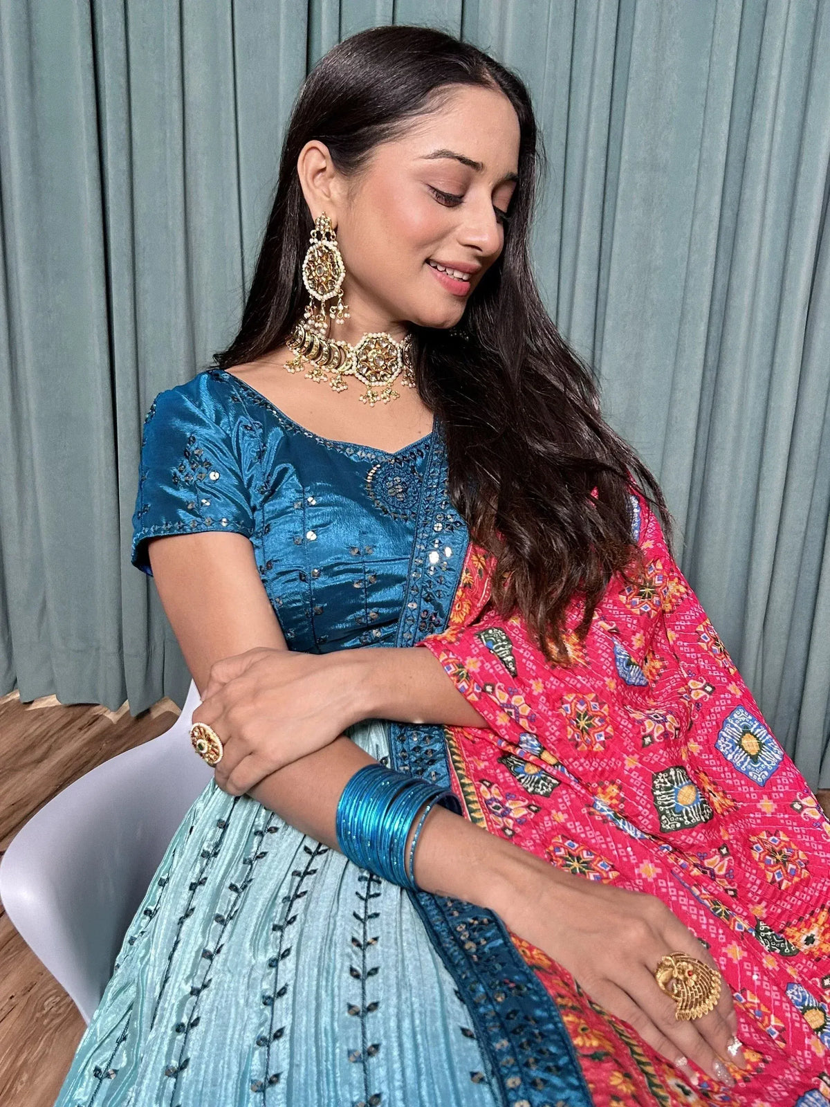 Woman in blue embroidered lehenga choli with pink printed dupatta, gold jewelry, and bangles
