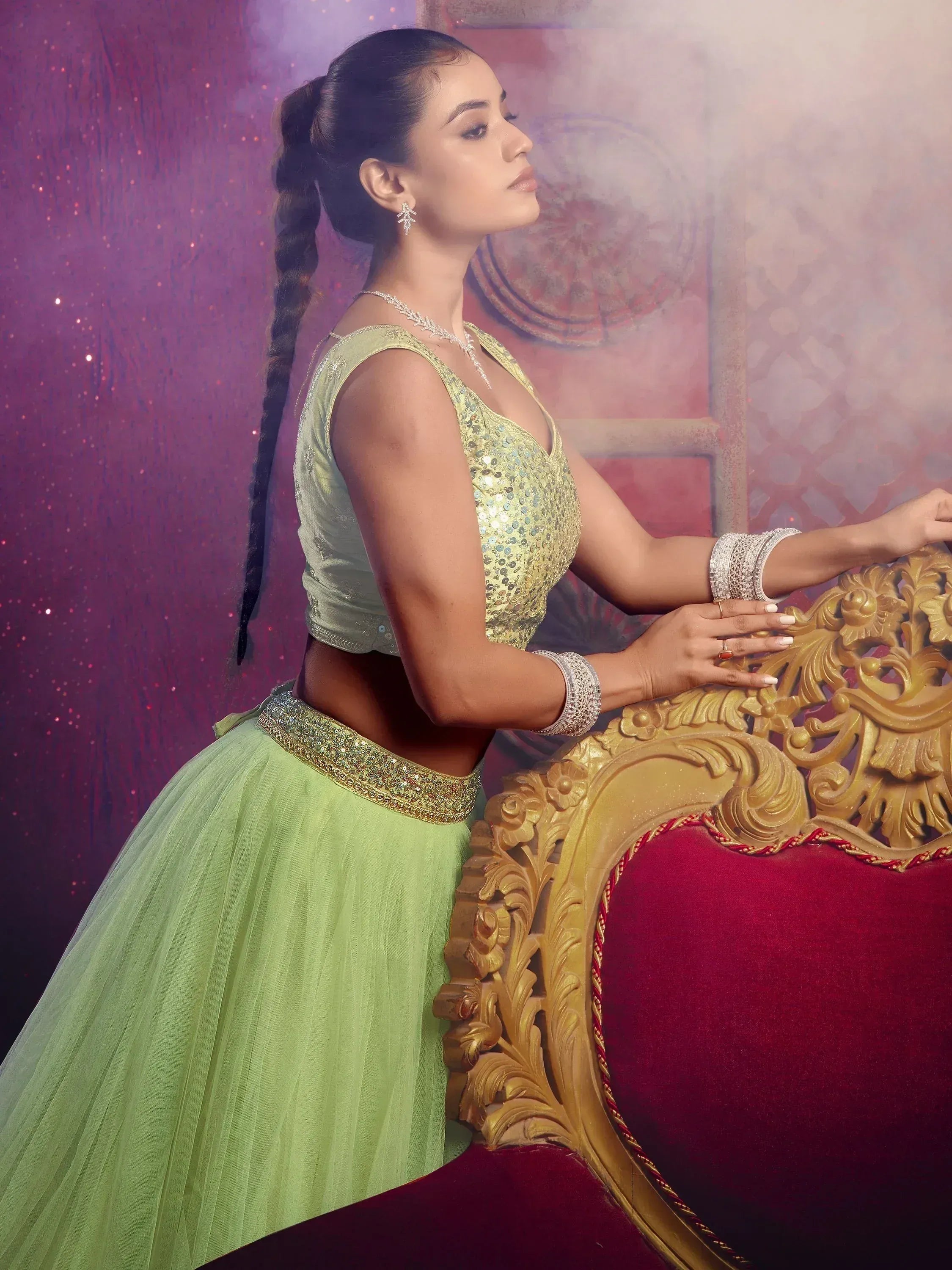 Woman in mint green sequin lehenga choli with gold embroidery, posing beside ornate golden chair