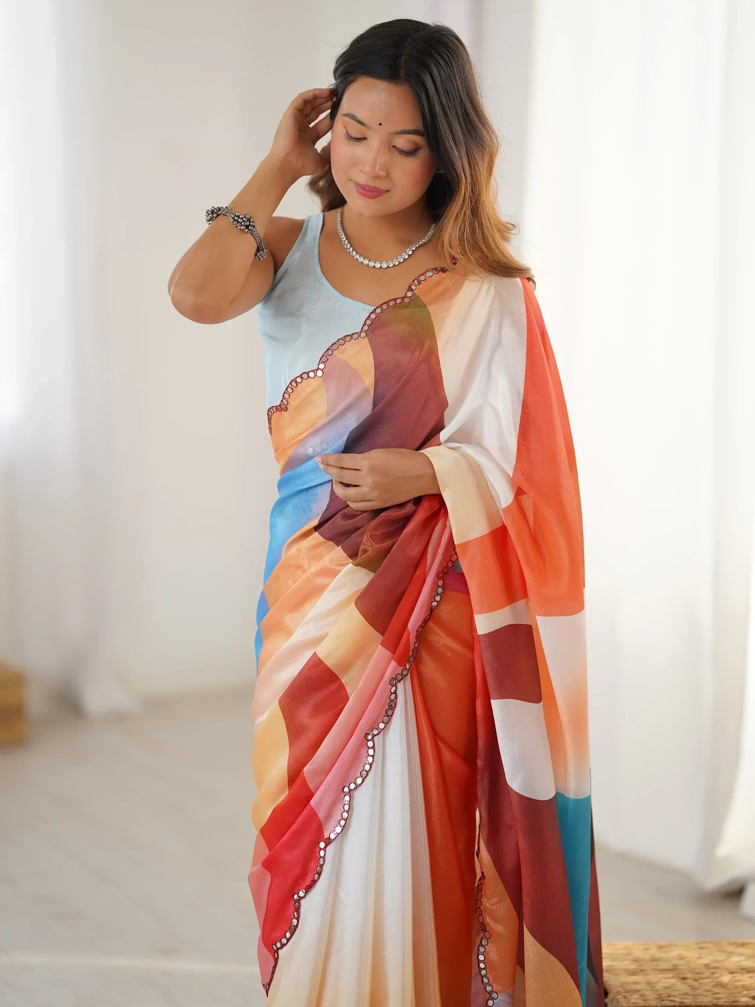 Woman in colorful geometric print saree with mirror work, paired with light blue blouse, ethnic wear