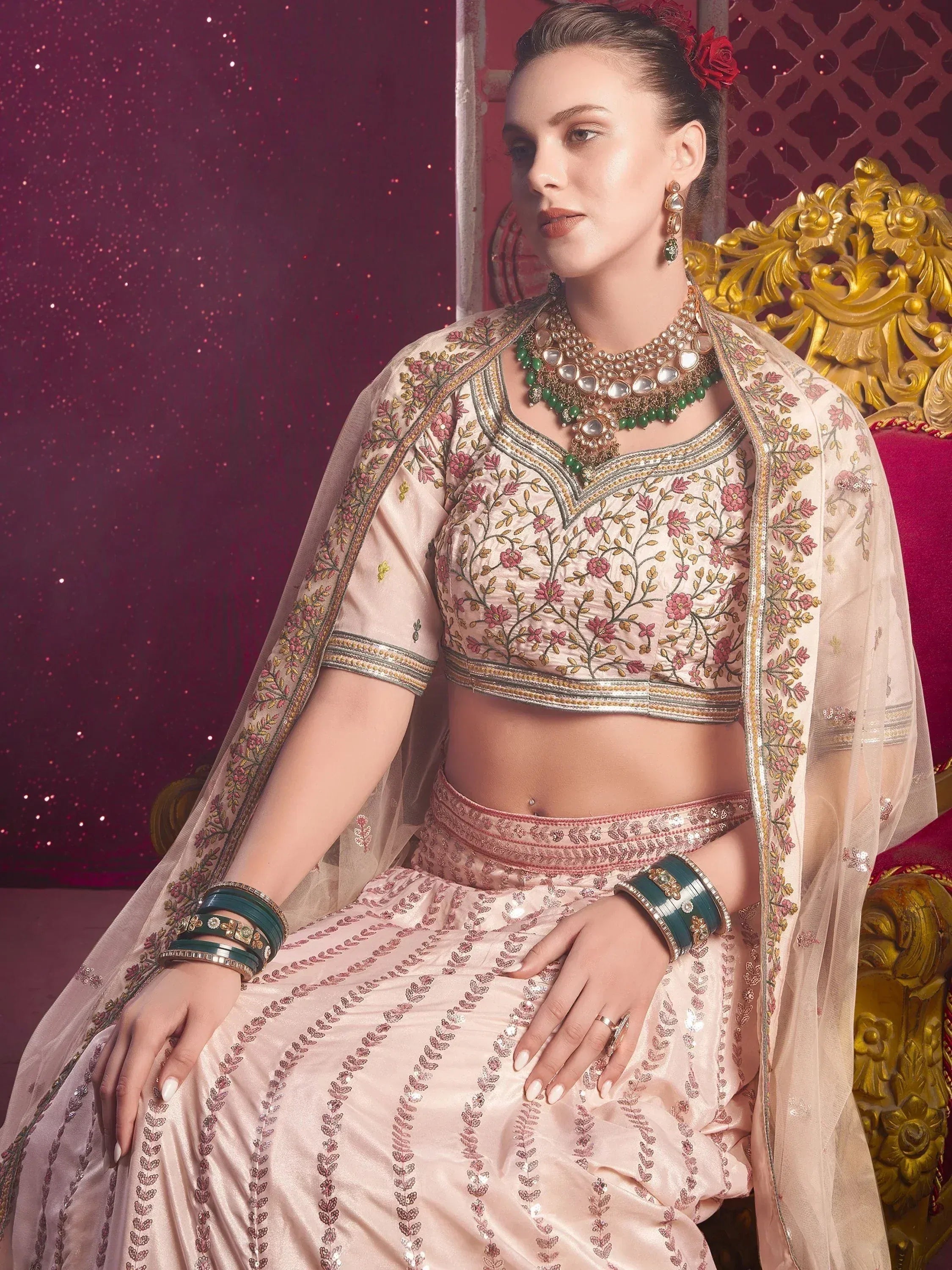 Elegant pink embroidered lehenga choli with floral motifs, paired with green jewelry and dupatta, perfect for Indian ethnic wear.