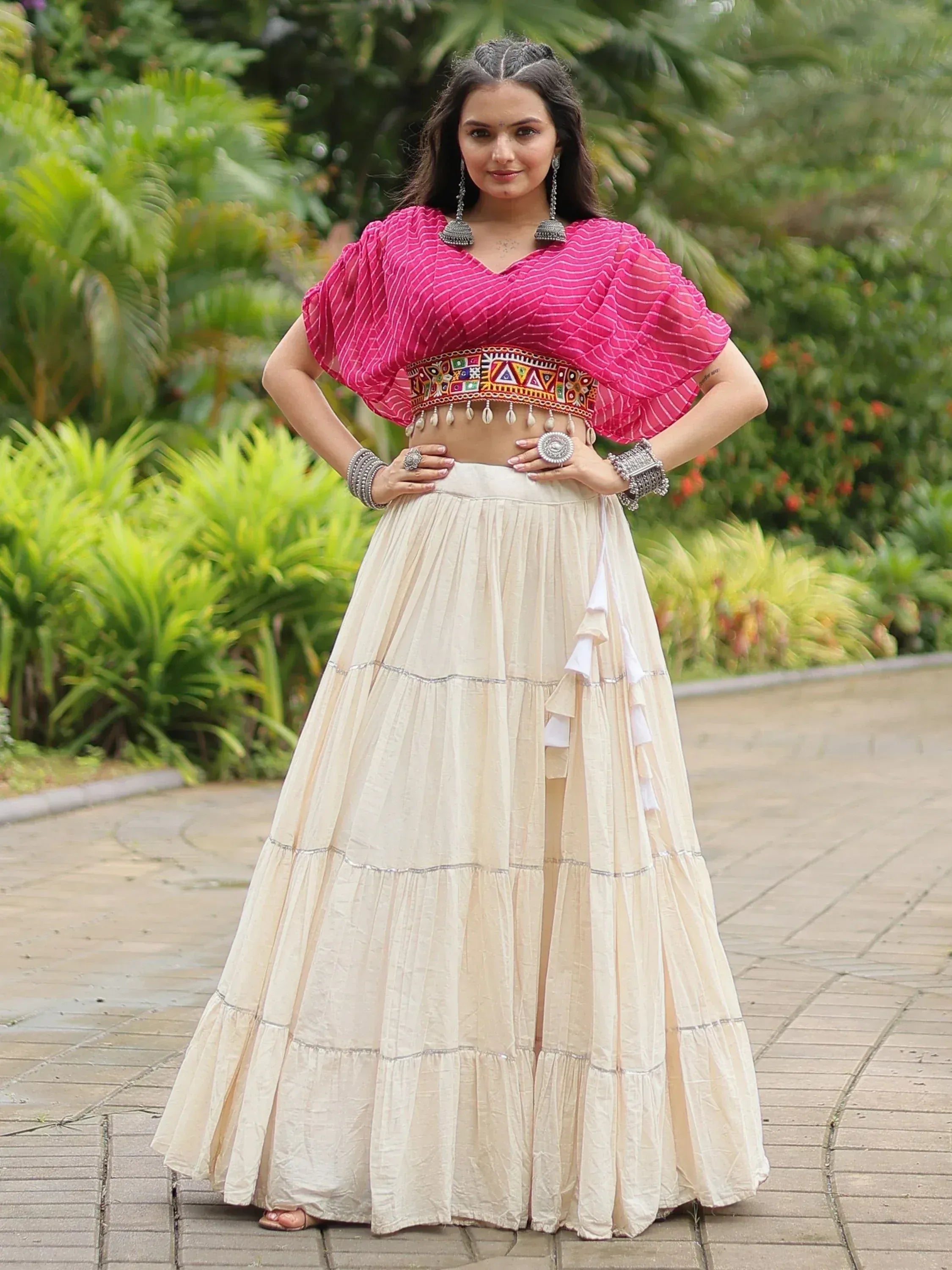 Woman in pink striped crop top and cream tiered skirt, Indian ethnic wear with mirror work, garden setting