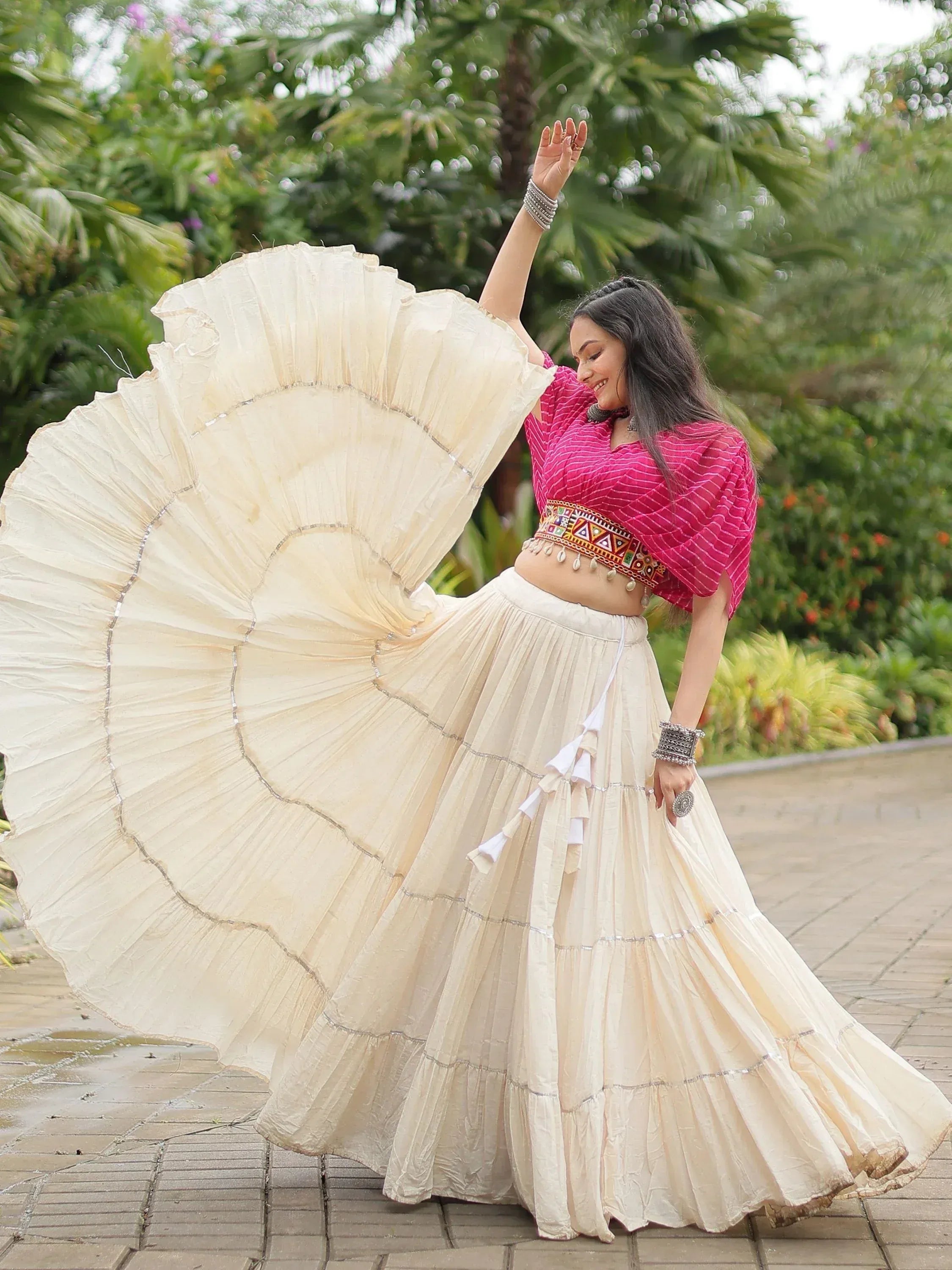 Woman twirling in cream pleated skirt with pink blouse, ethnic Indian wear for festive occasions