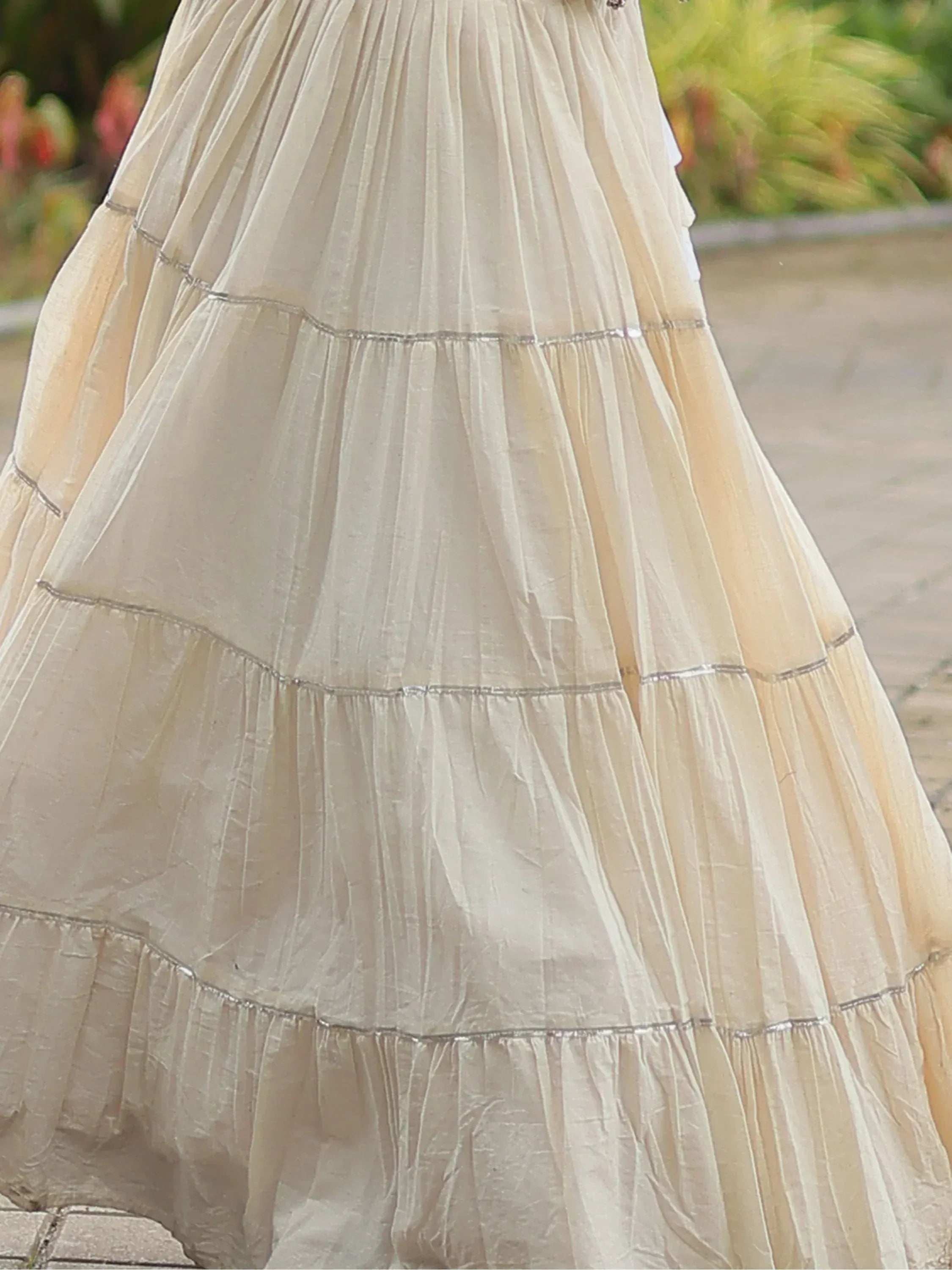 Cream tiered ethnic gown with pleated layers and silver trim, perfect for Indian occasions