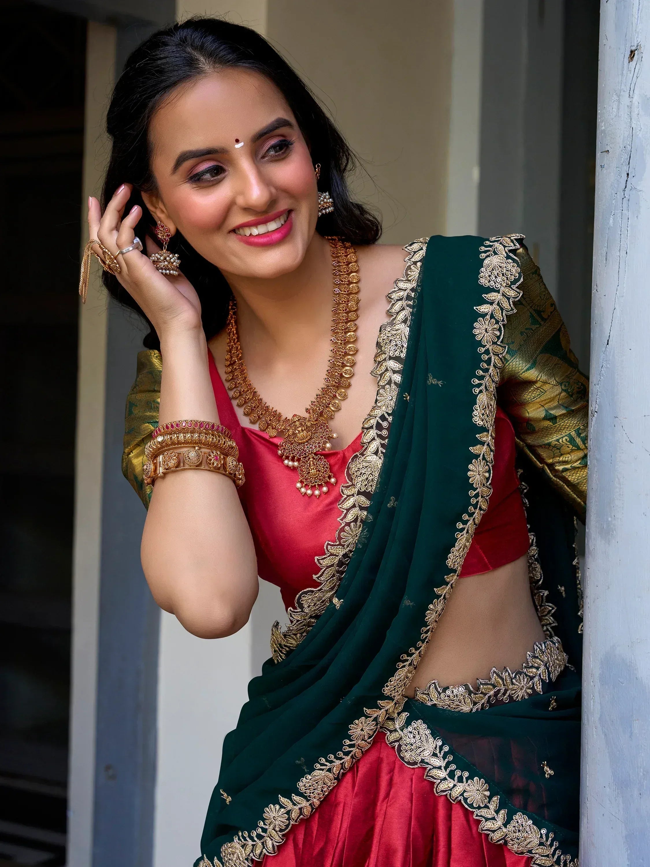 Woman in red and green embroidered saree with gold jewelry, traditional Indian ethnic wear
