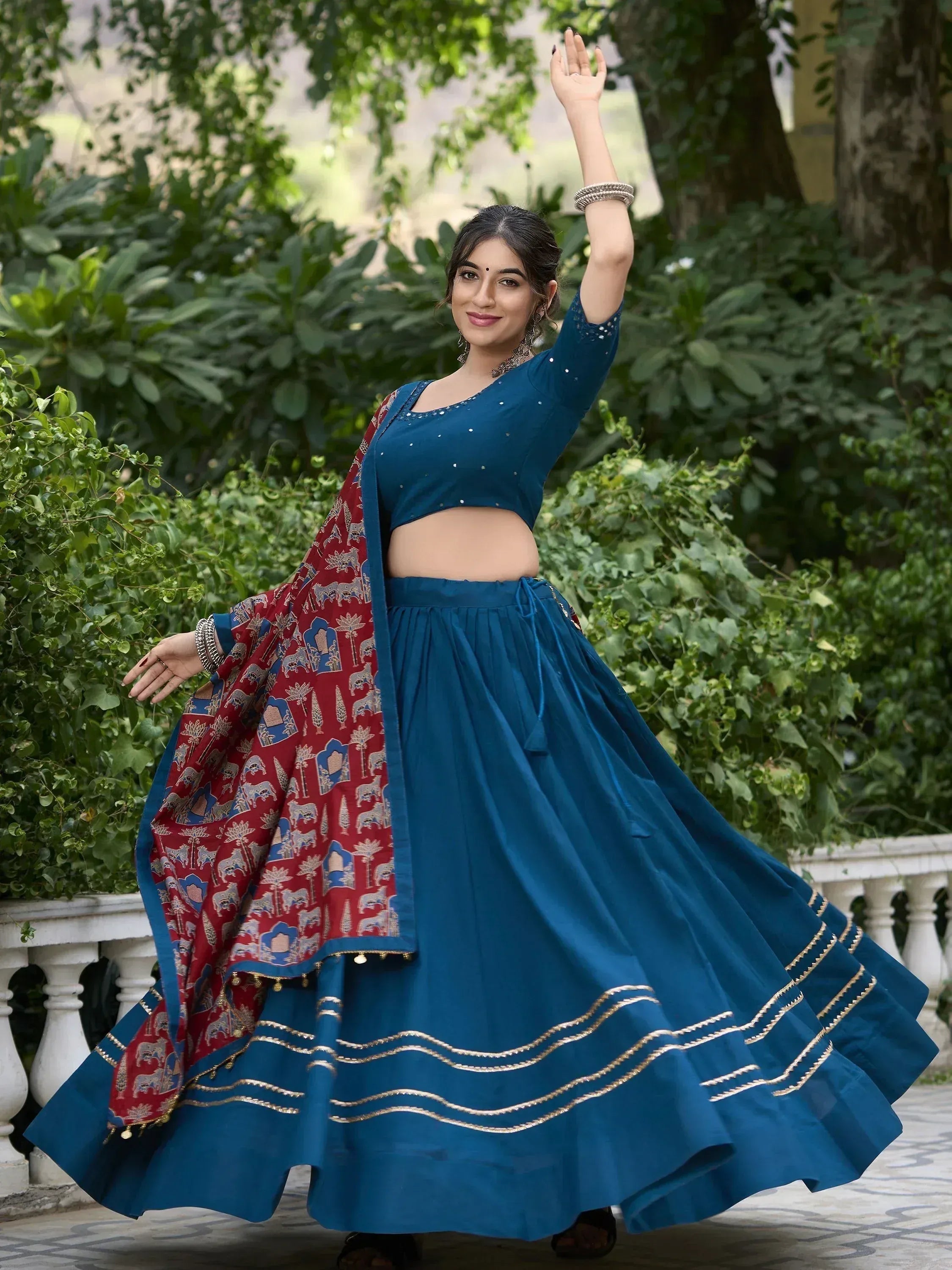 Woman in blue lehenga choli with red printed dupatta, gold embroidery, dancing outdoors