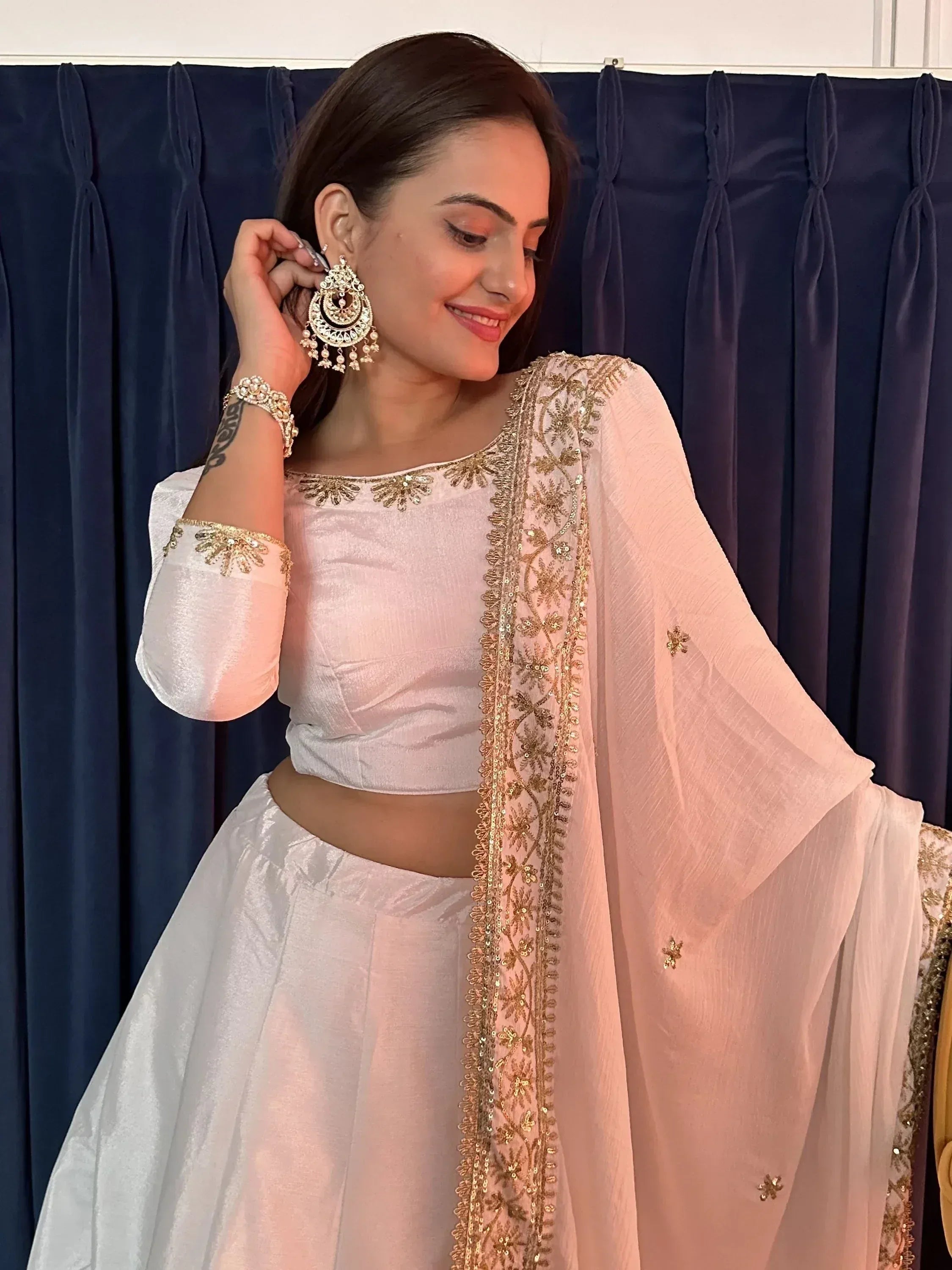 Woman in white ethnic lehenga choli with gold embroidery and jhumka earrings, perfect for Indian weddings or festivals.