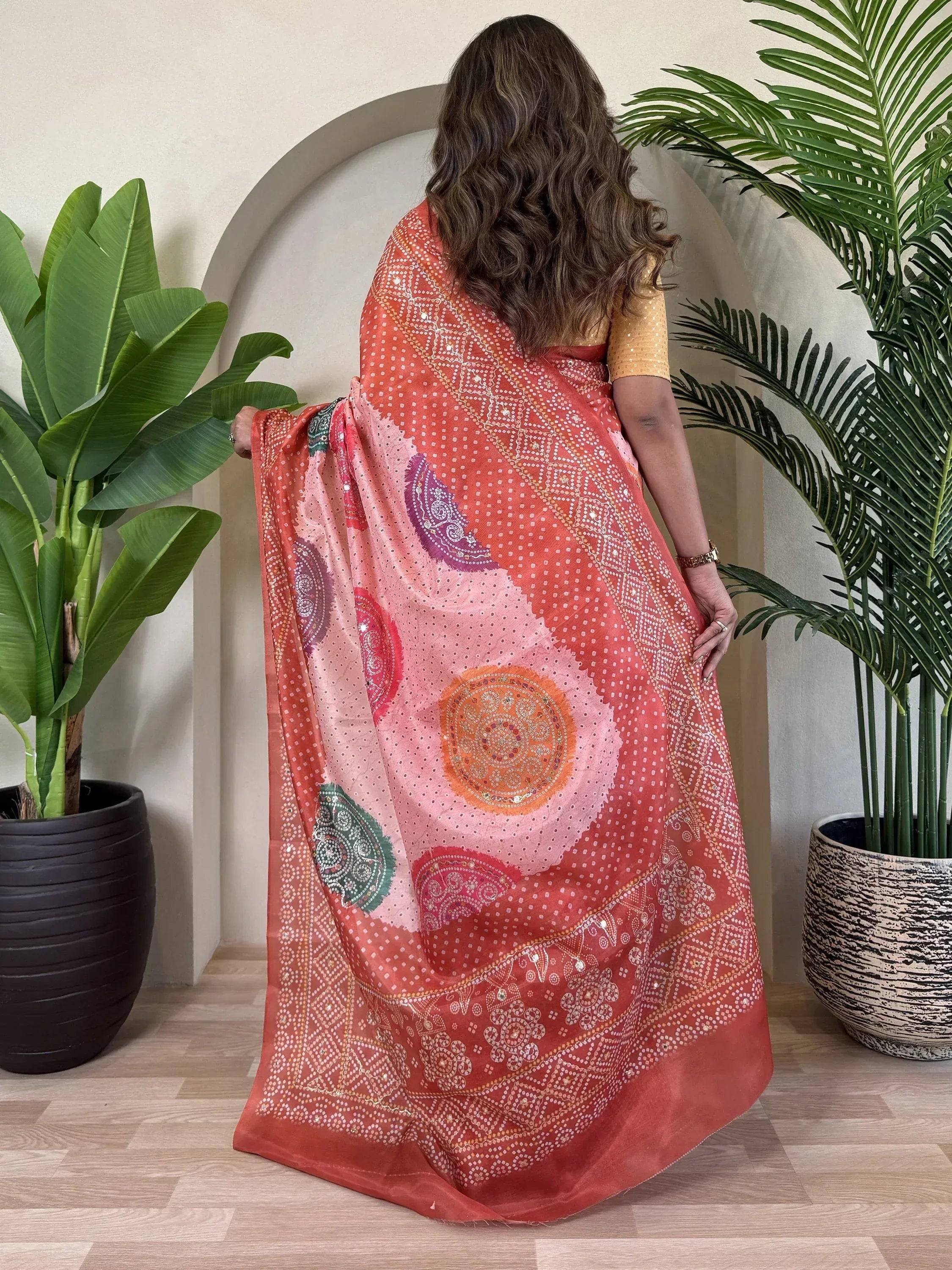 Woman wearing coral pink ethnic saree with mirror work and paisley print, styled with gold blouse