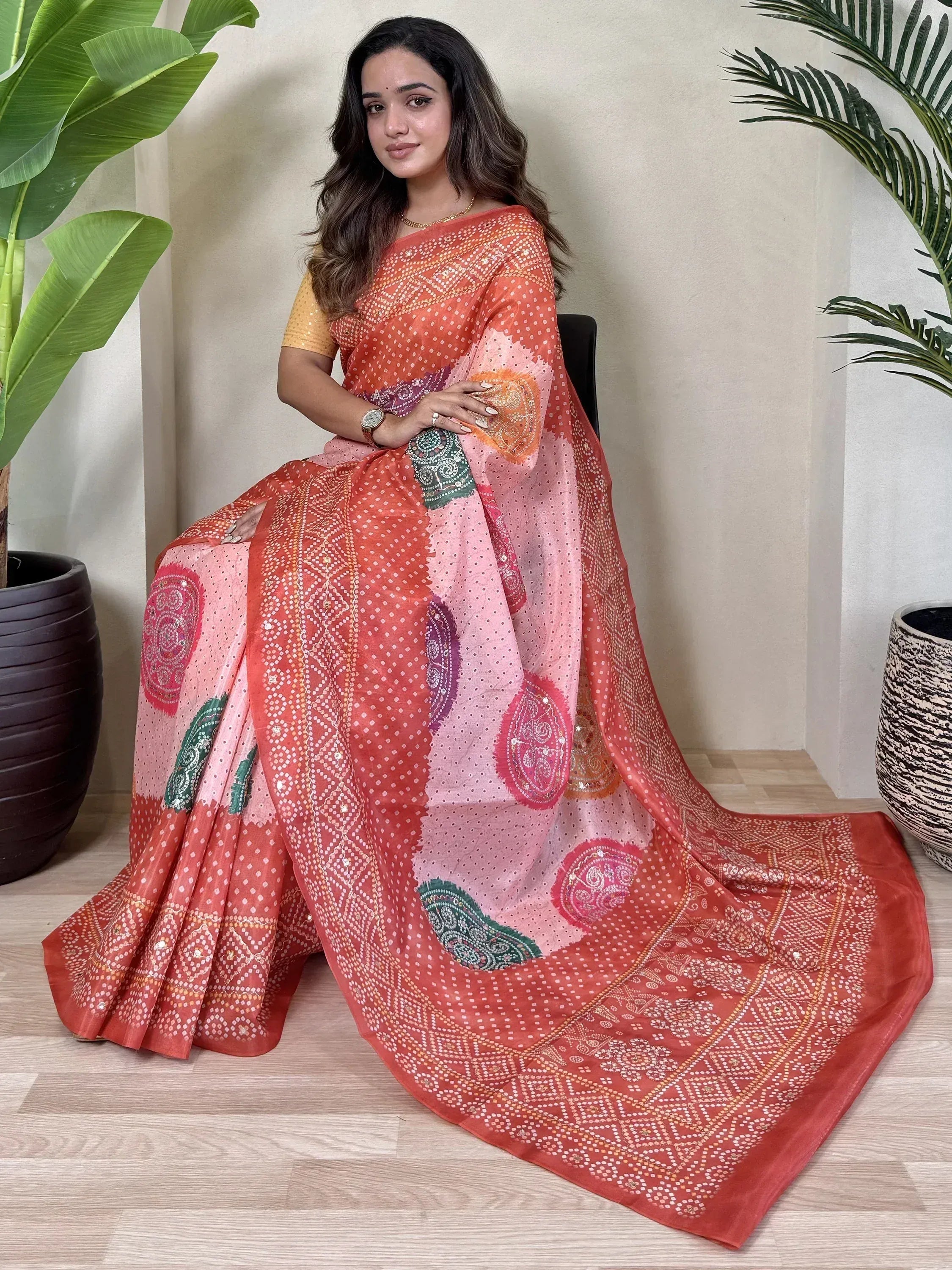 Woman in vibrant orange and pink printed saree with paisley motifs, perfect for Indian ethnic wear occasions.