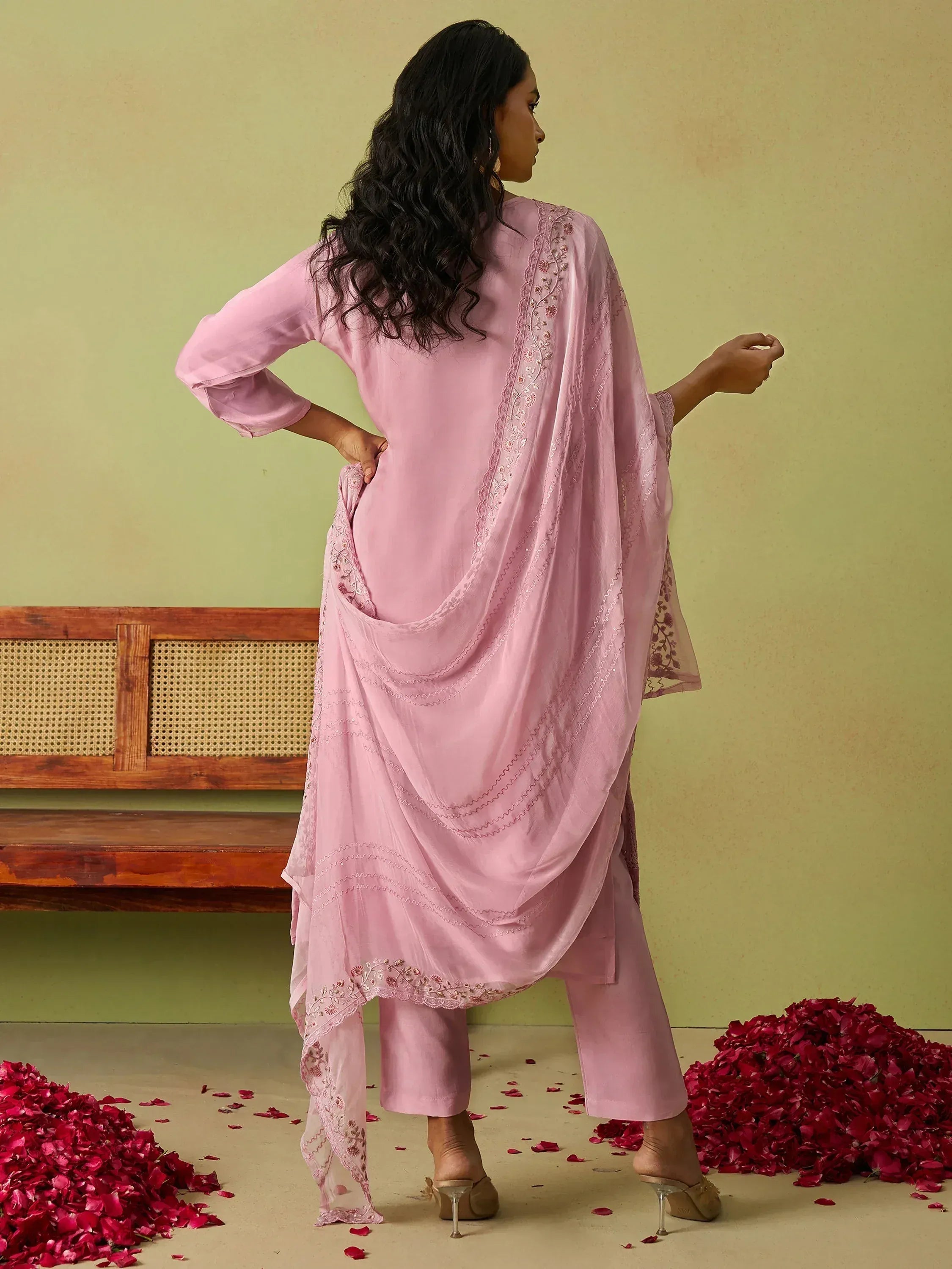 Pink embroidered salwar kameez with sheer dupatta, styled with rose petals and wooden bench