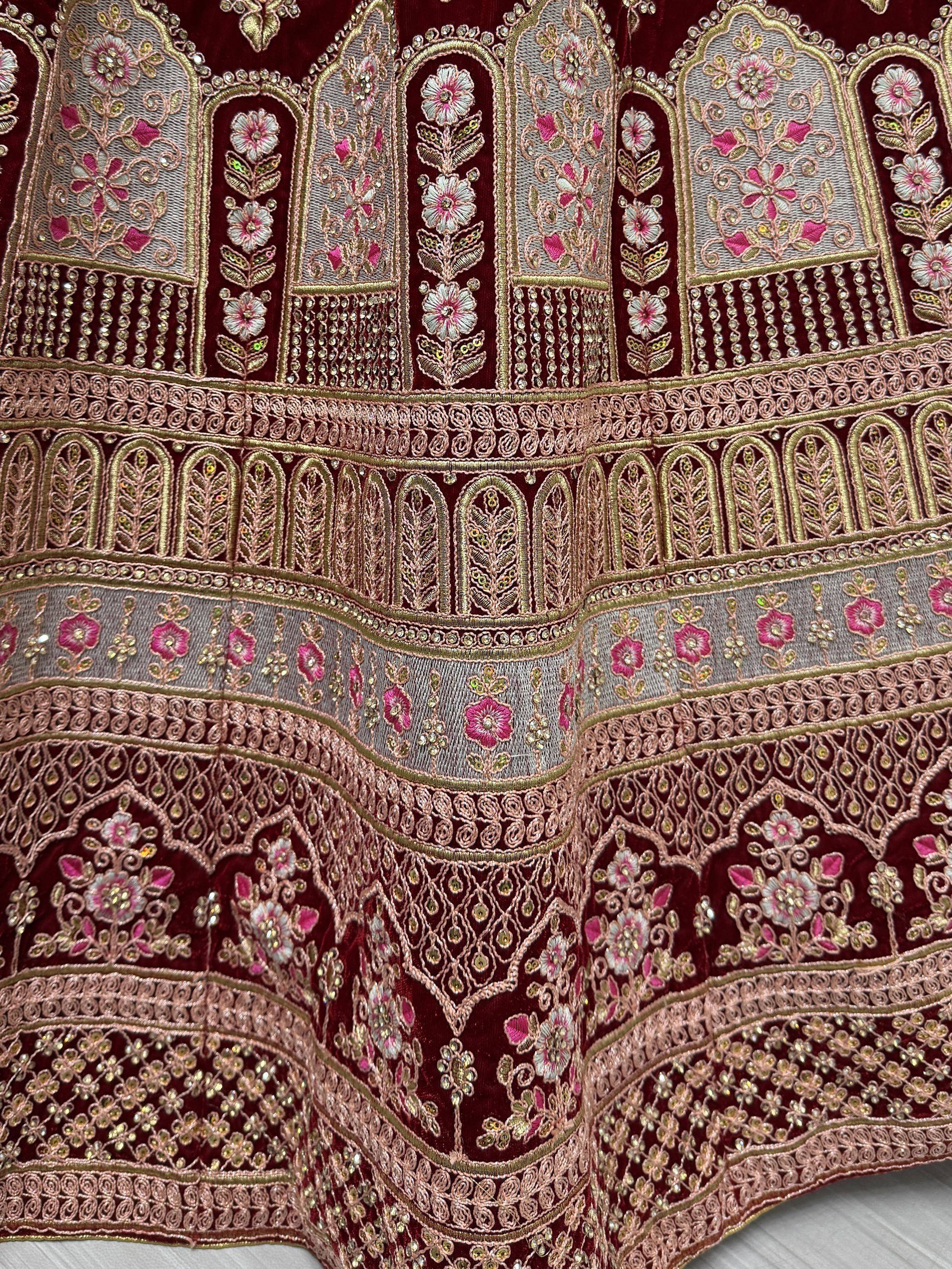 Luxury maroon velvet lehenga with intricate floral embroidery and gold zari work, perfect for Indian weddings.