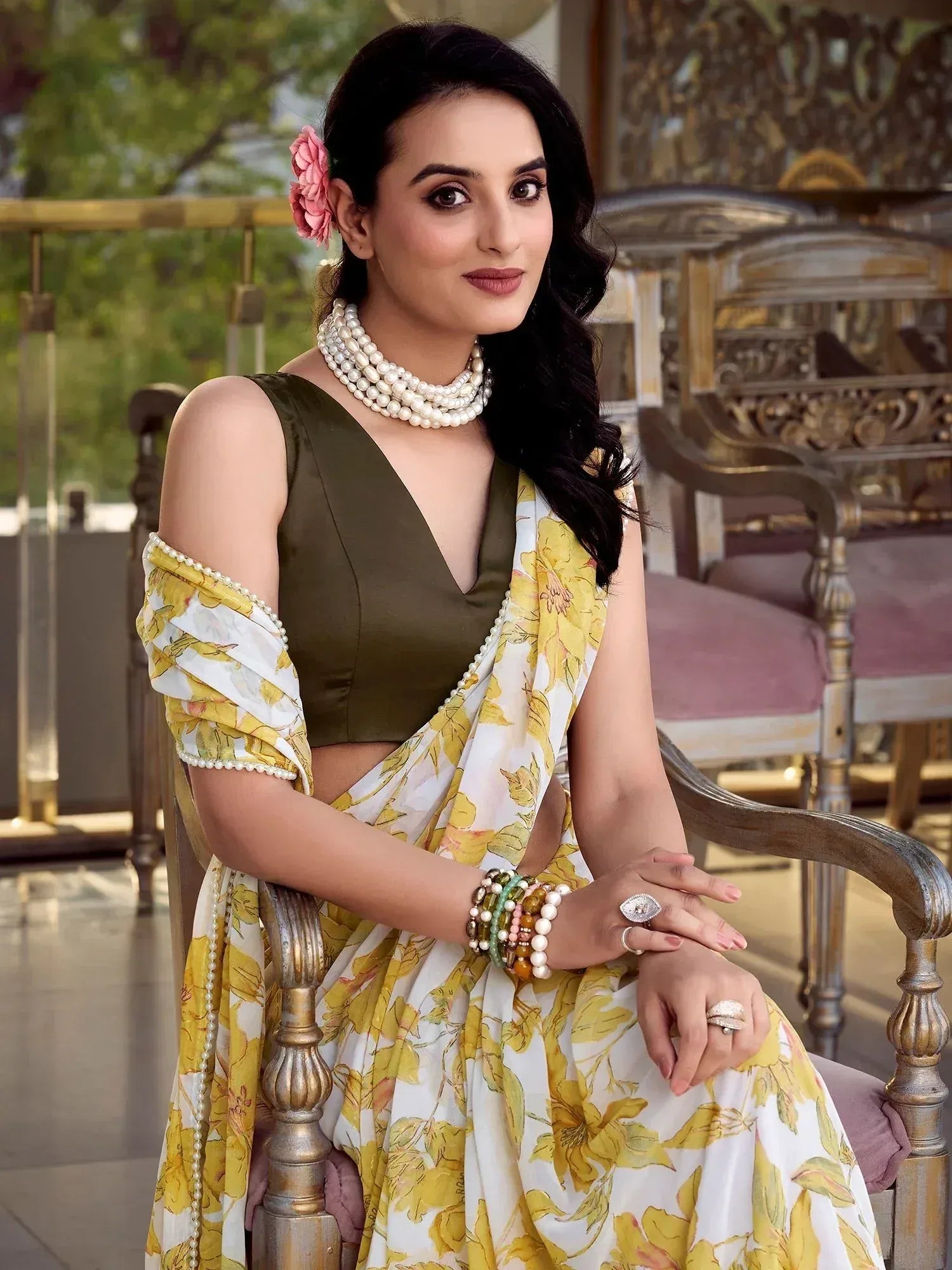Woman in olive green blouse with yellow floral saree, pearl jewelry, and pink hair flower