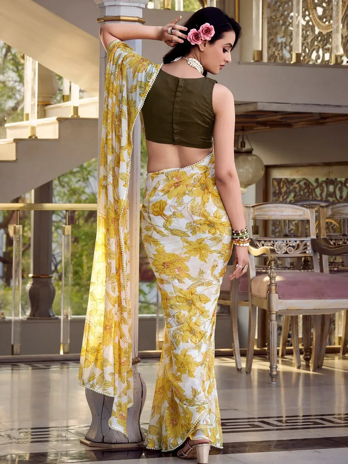 Woman in yellow floral saree with olive green blouse, pearl trim, and pink hair flowers
