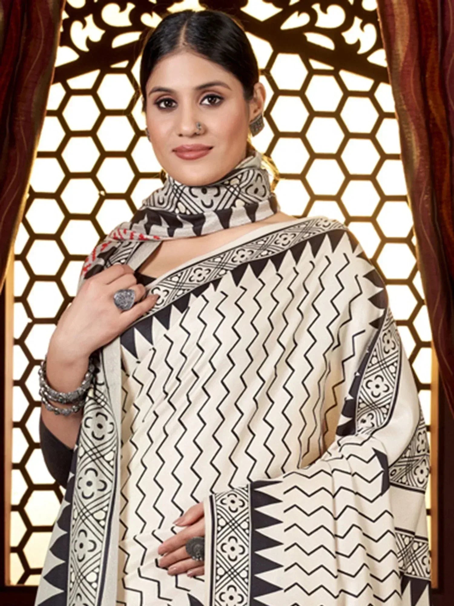 Woman in vibrant printed saree with orange blouse, ethnic jewelry, and traditional nose ring