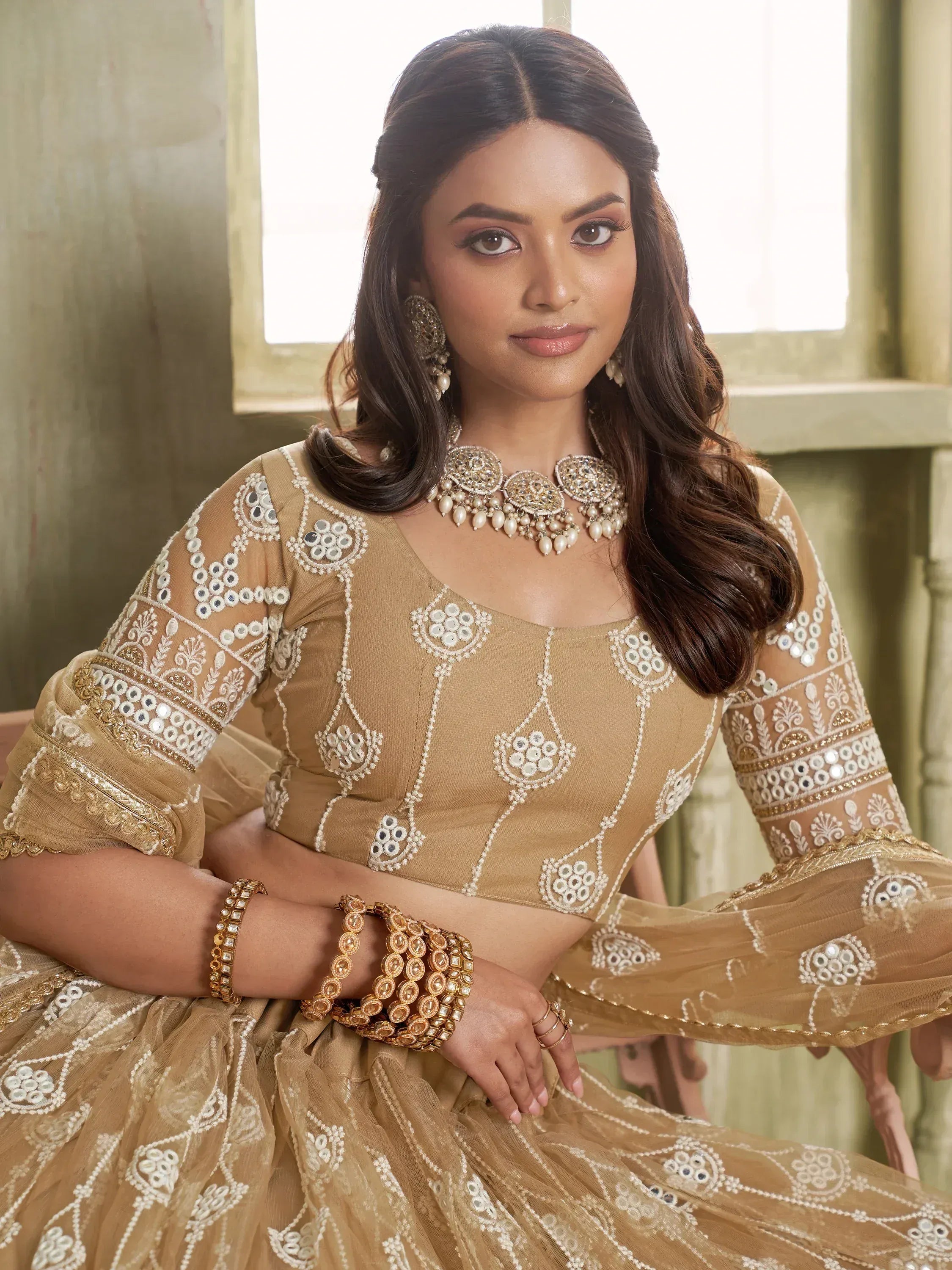 Elegant beige lehenga choli with mirror work and gold embroidery, perfect for Indian ethnic wear occasions.