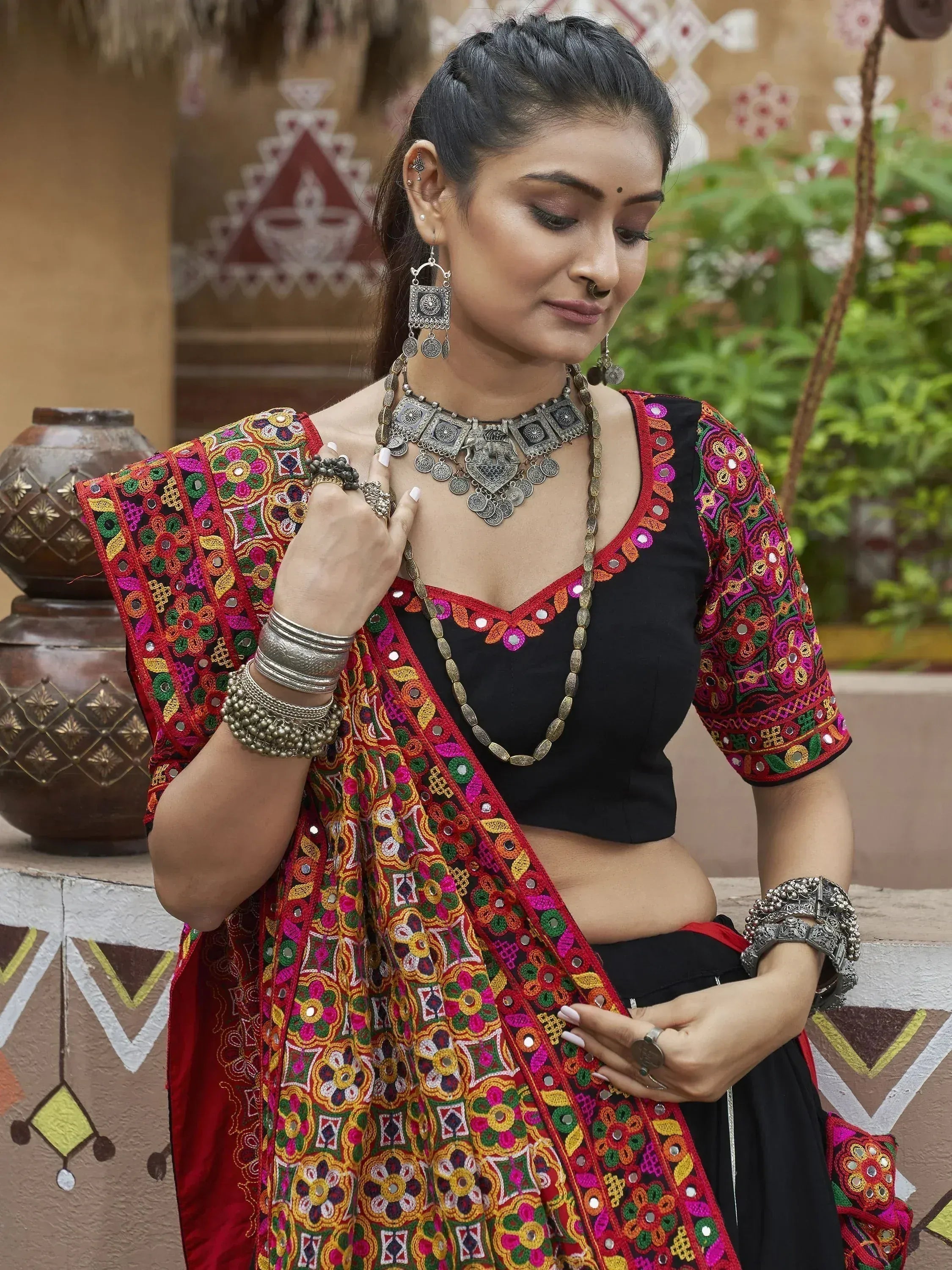 Woman in vibrant embroidered Indian ethnic wear with mirror work, traditional jewelry, and black blouse