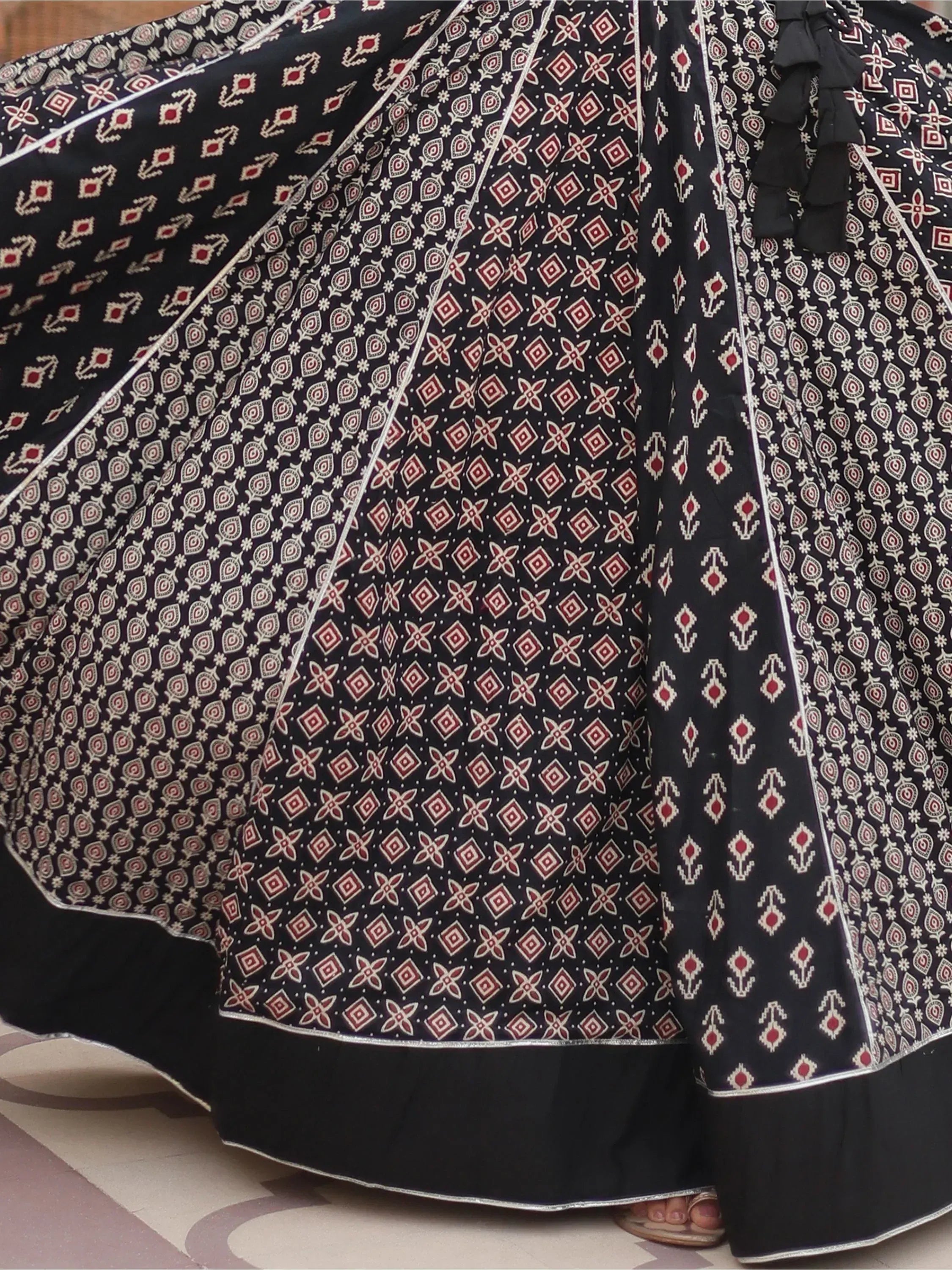 Black ethnic gown with red and white geometric print, ruffled detailing, and silver trim for festive occasions