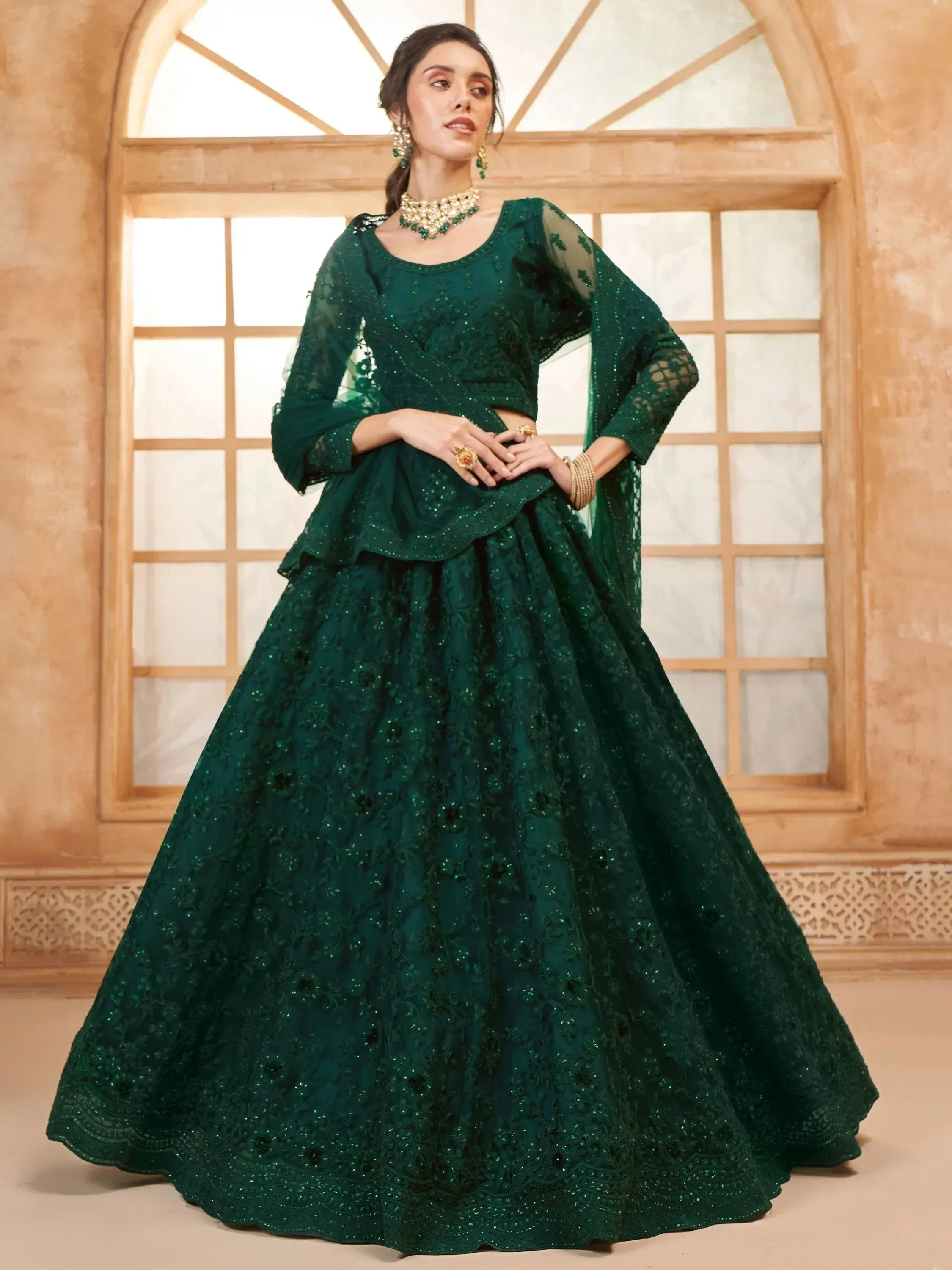 Emerald green designer lehenga choli with intricate embroidery and sheer sleeves, perfect for Indian weddings and festive occasions.