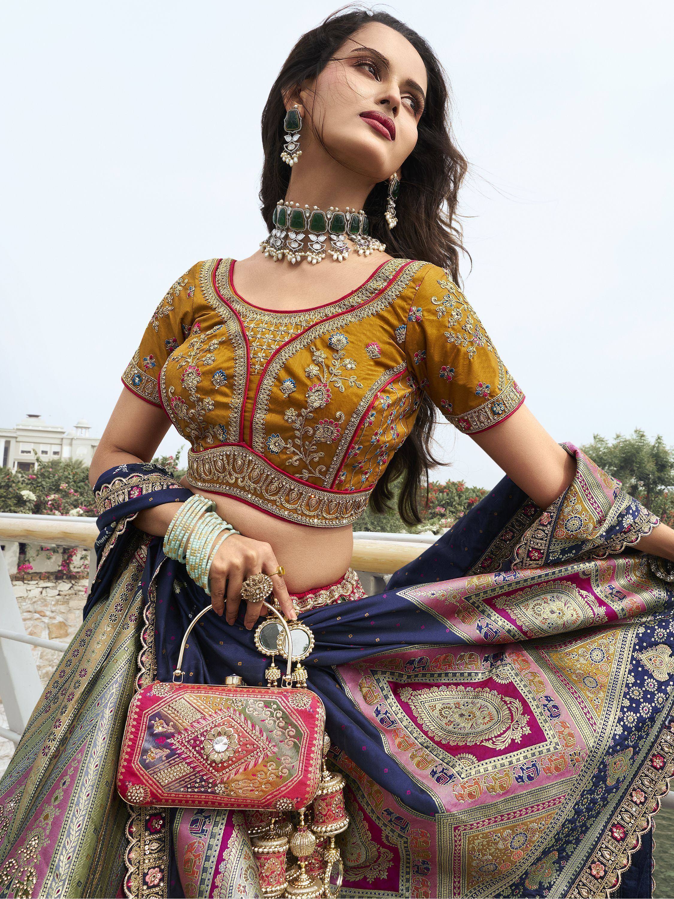 Woman in embroidered mustard blouse and navy pink lehenga with traditional jewelry and clutch