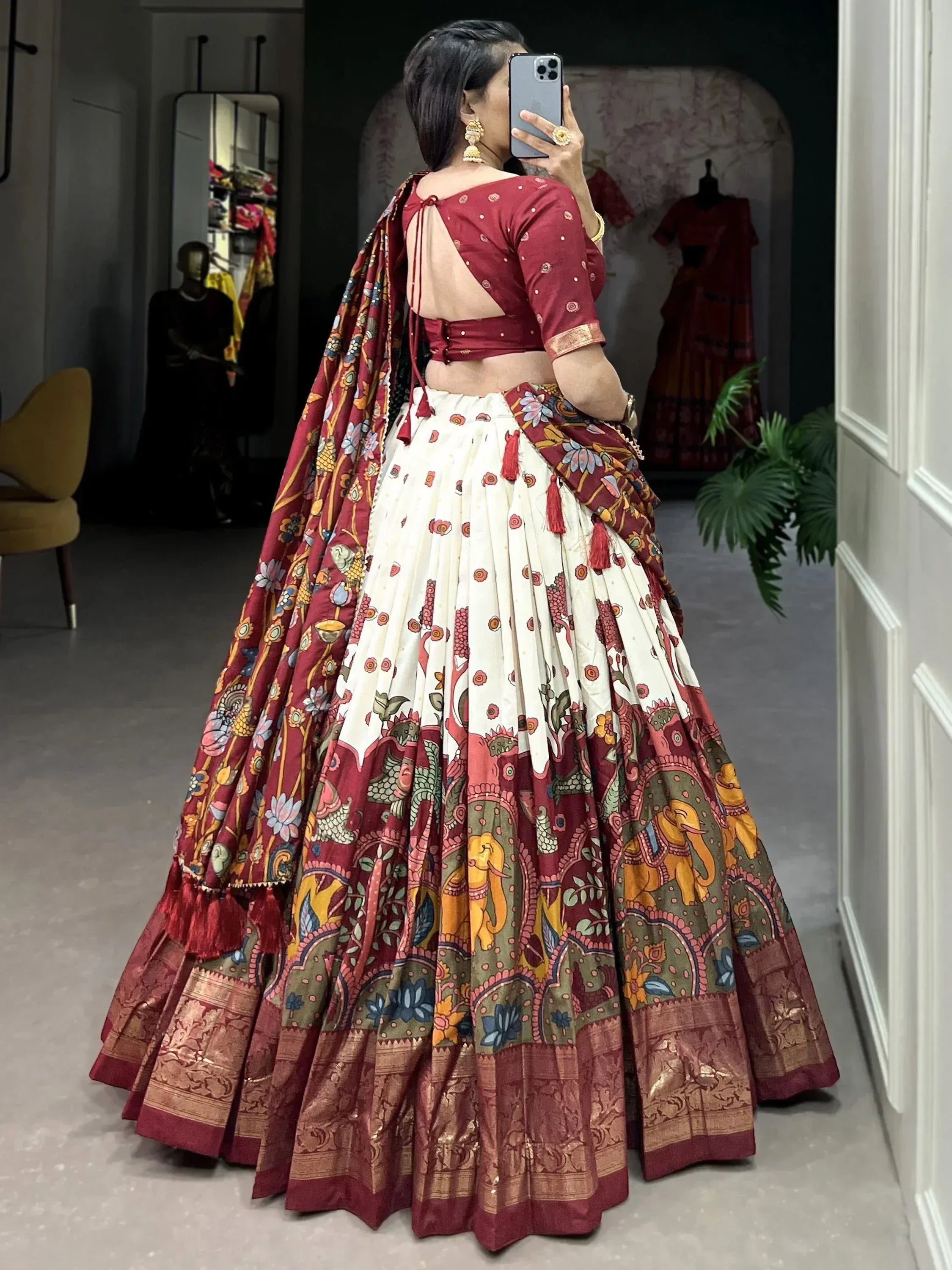 Woman in maroon and cream printed lehenga choli with elephant motifs, back view in boutique