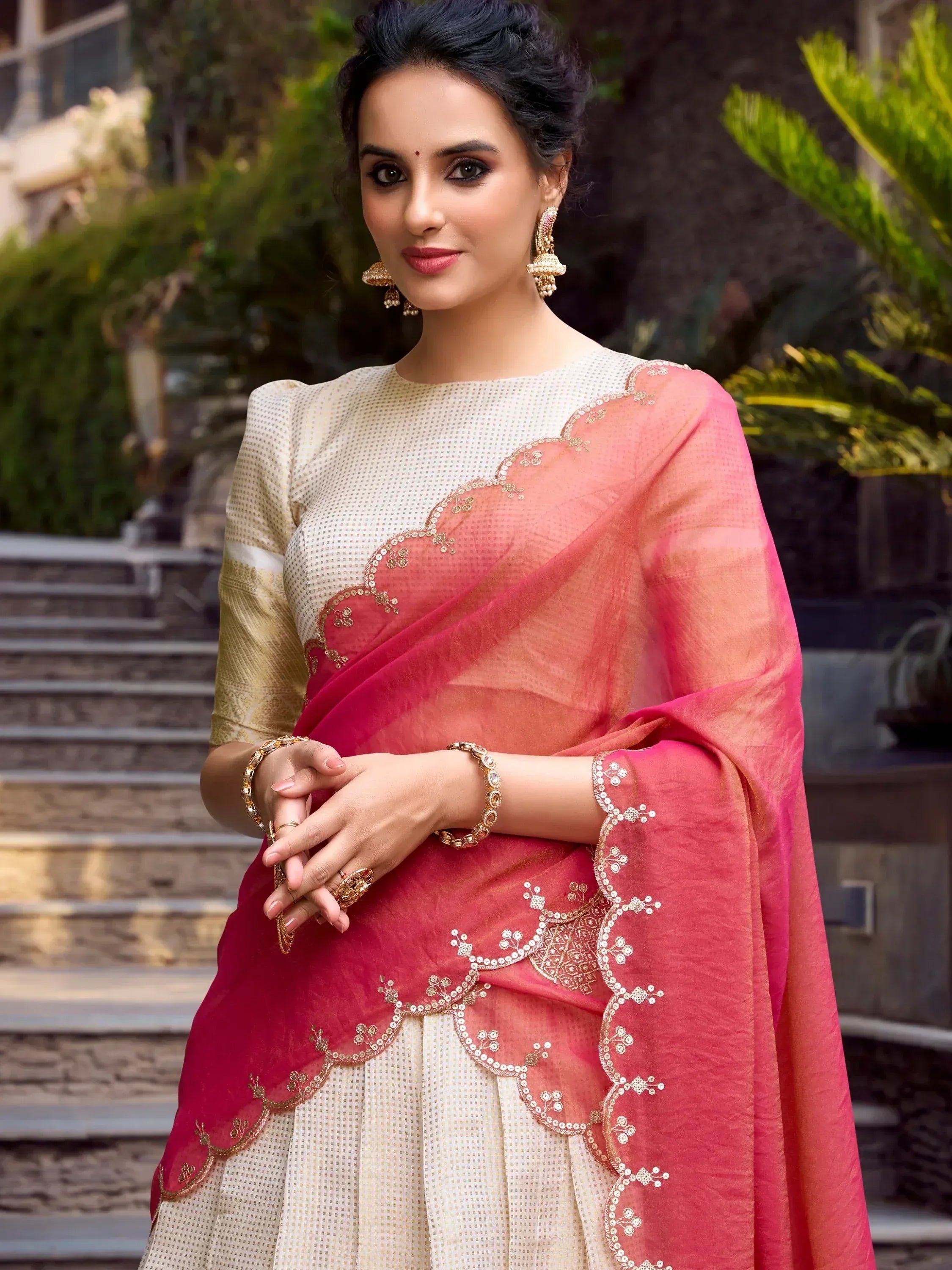 Woman in elegant pink and cream embroidered saree with gold jewelry, perfect for Indian ethnic occasions