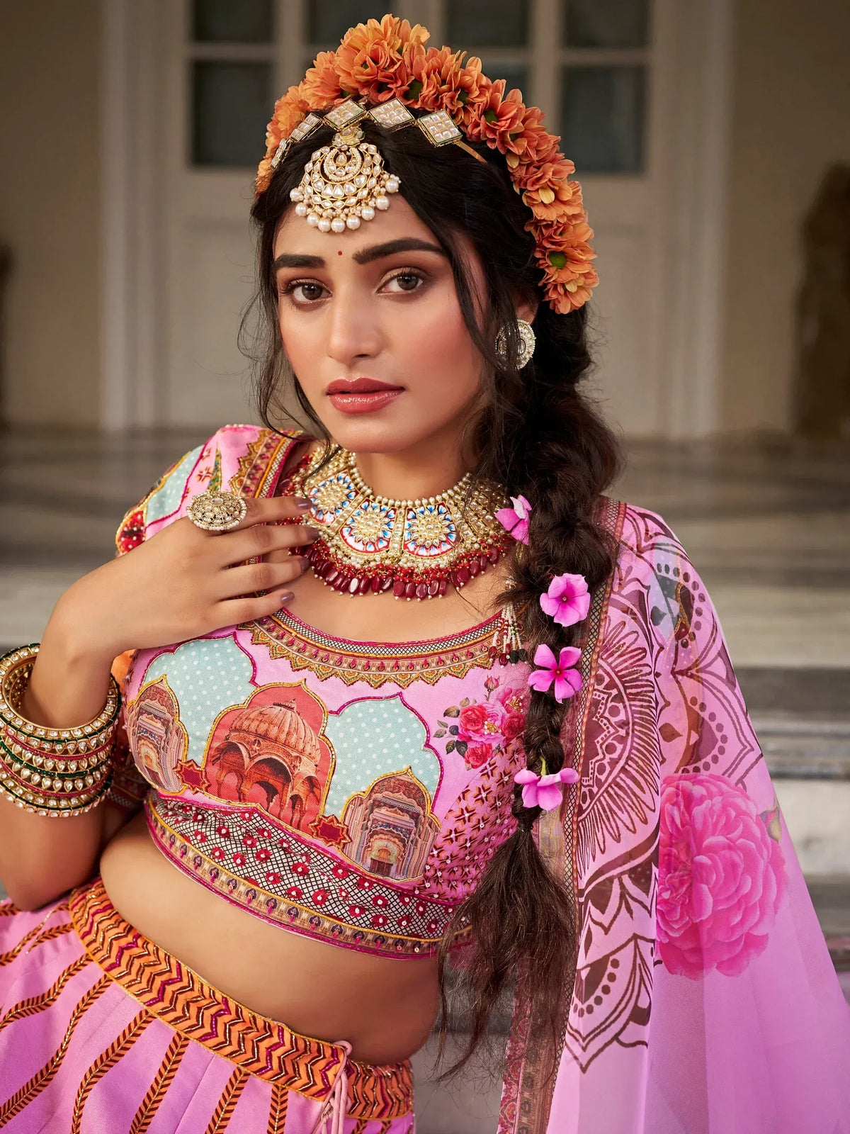 Woman in vibrant pink Indian lehenga choli with floral crown, temple print blouse, and traditional jewelry