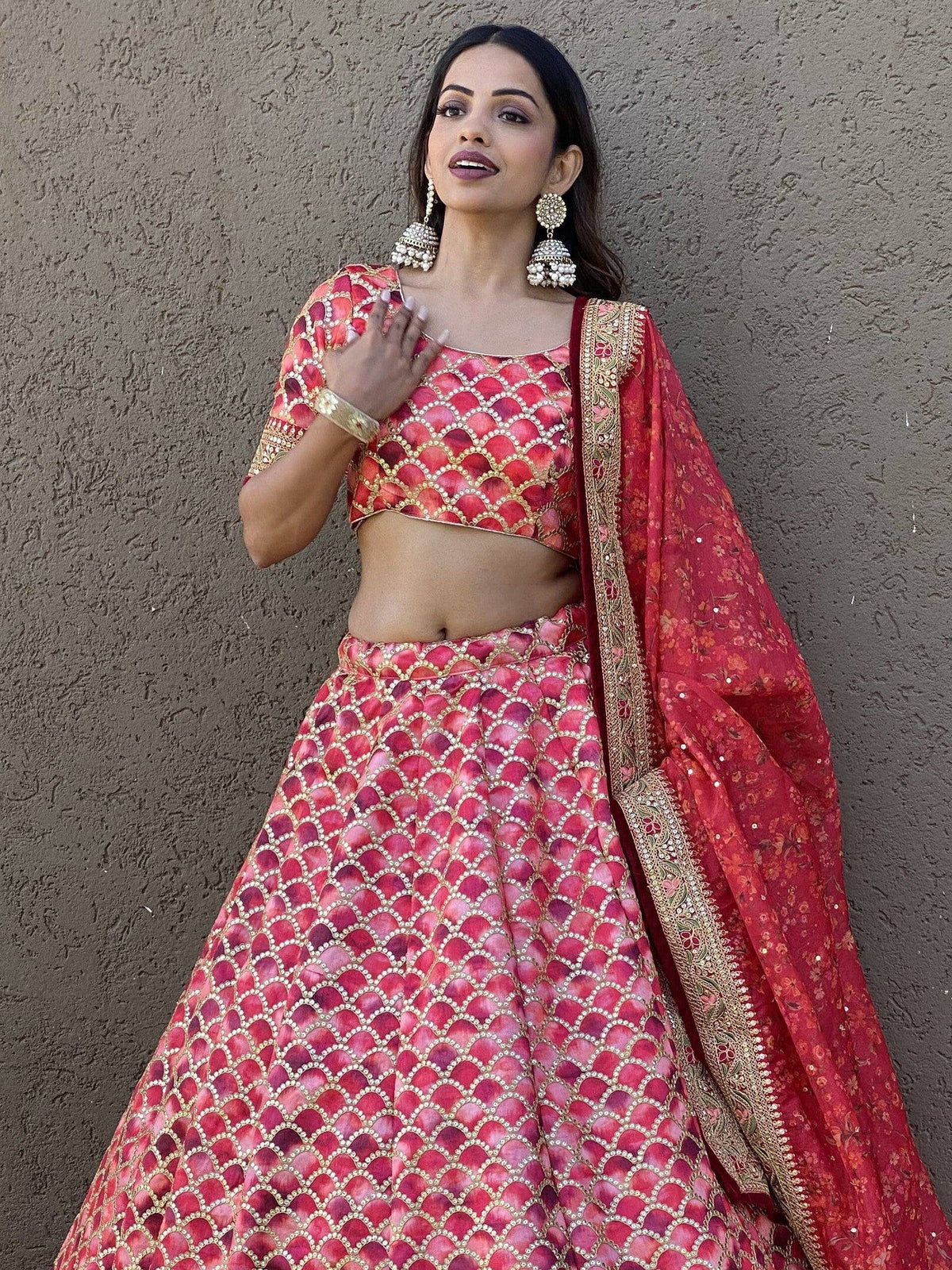 Red and pink designer lehenga choli with gold embroidery and floral dupatta, perfect for Indian weddings or festivals.