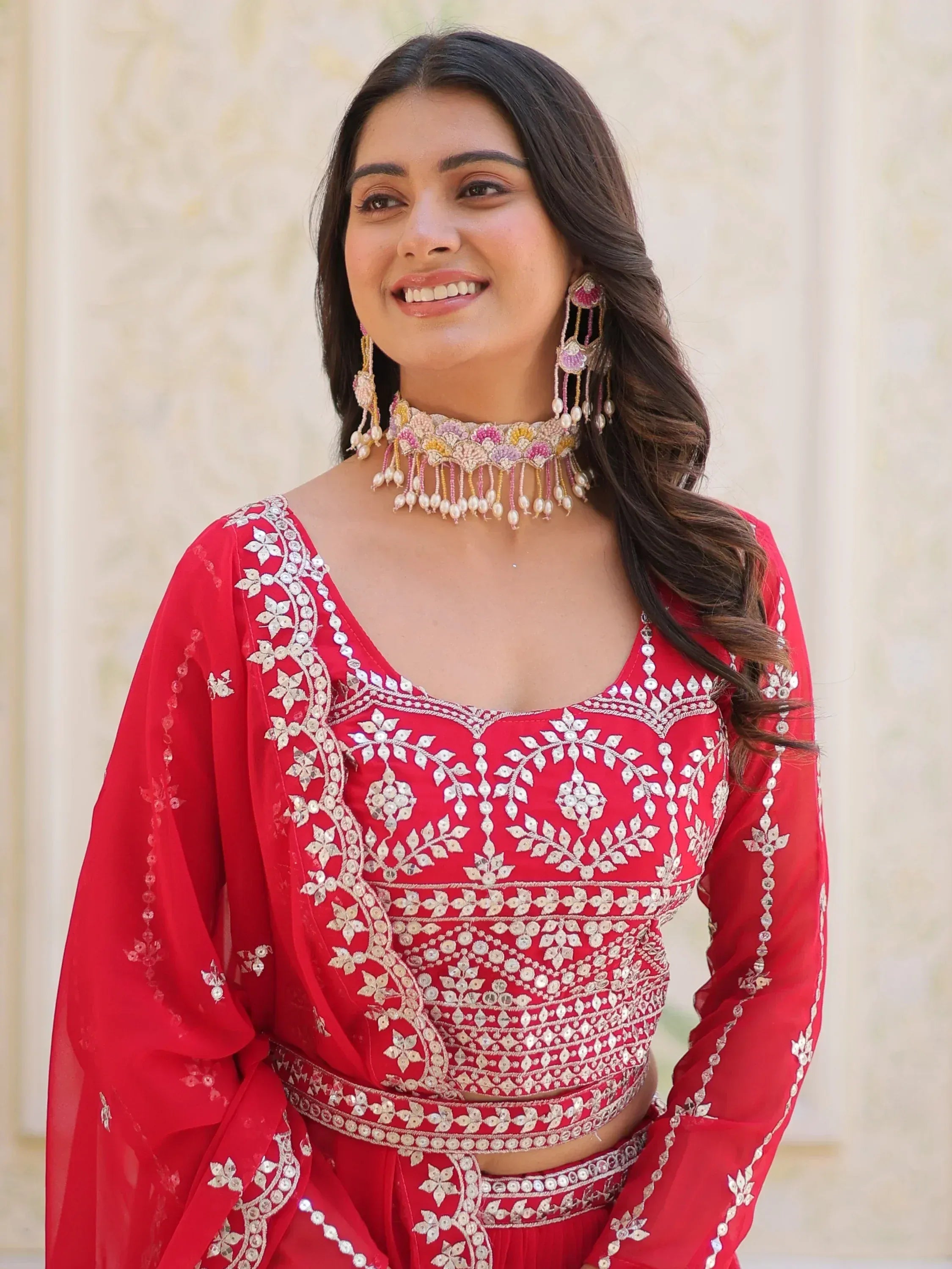 Red embroidered lehenga choli with mirror work, paired with floral jewelry for Indian ethnic wear