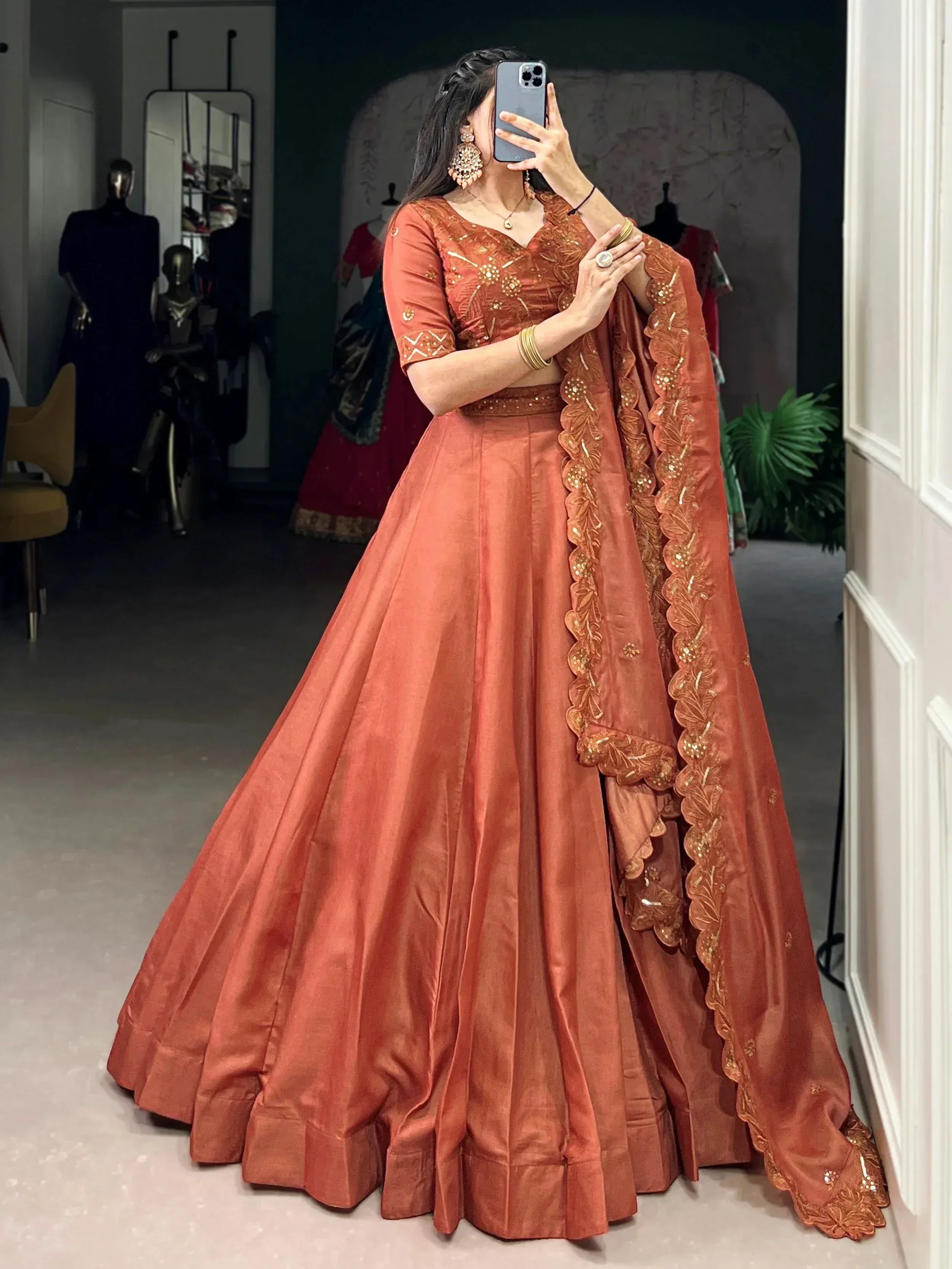 Woman in rust orange designer lehenga choli with gold embroidery, perfect for weddings and festive occasions.