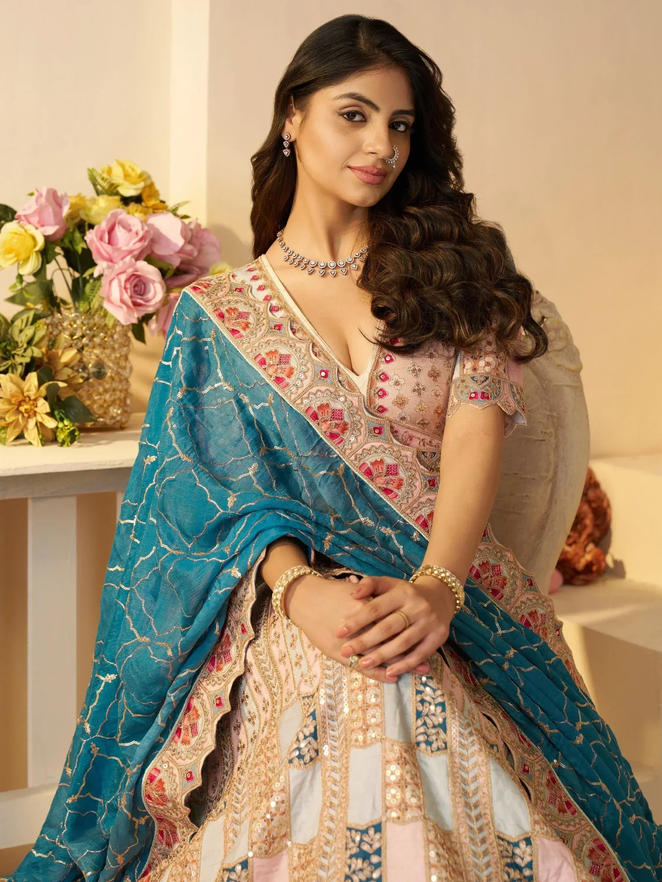 Woman in designer lehenga choli with teal dupatta, floral embroidery, and gold detailing for Indian ethnic wear