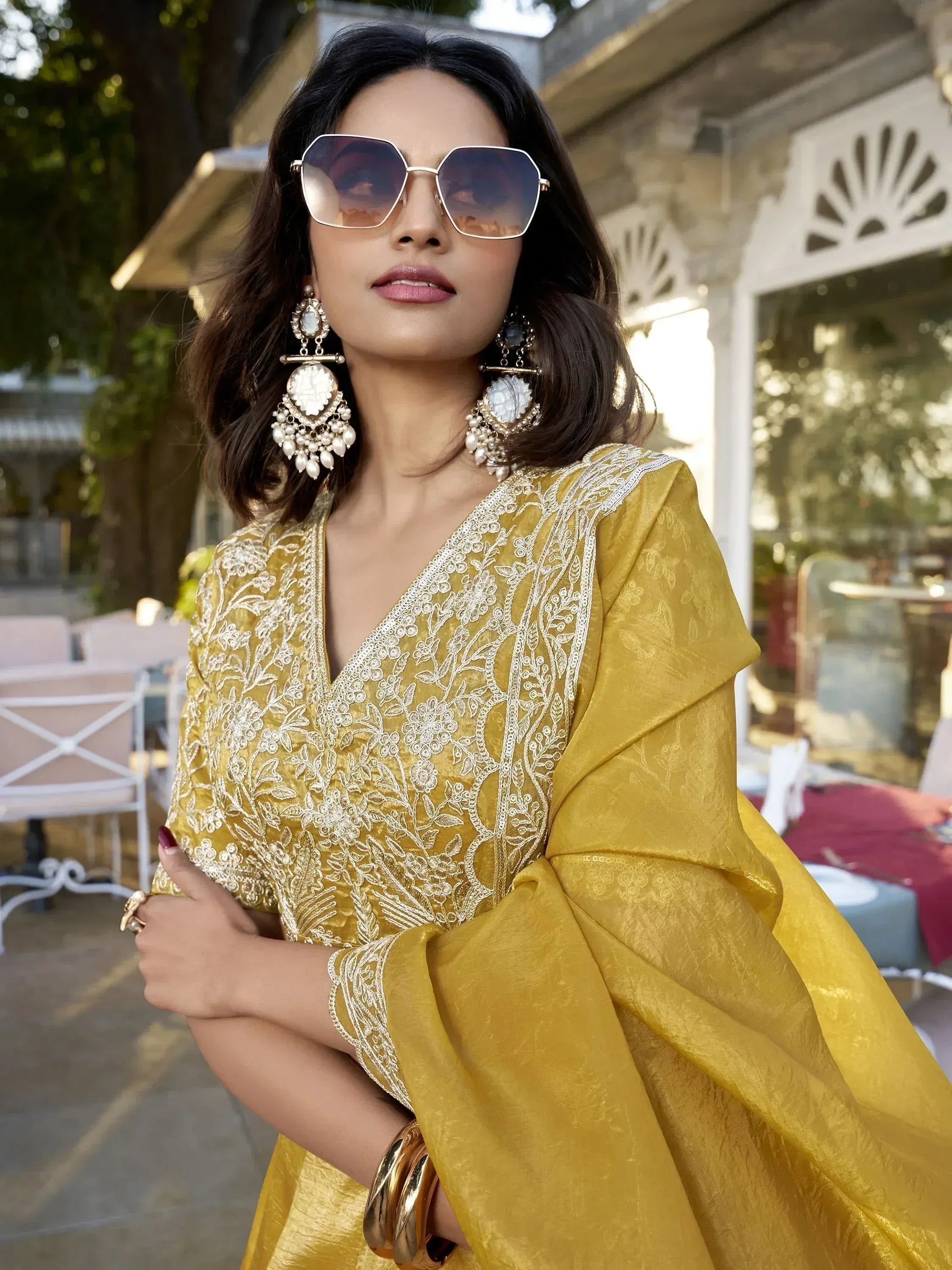 Yellow embroidered ethnic gown with white floral detailing, styled with statement earrings and sunglasses