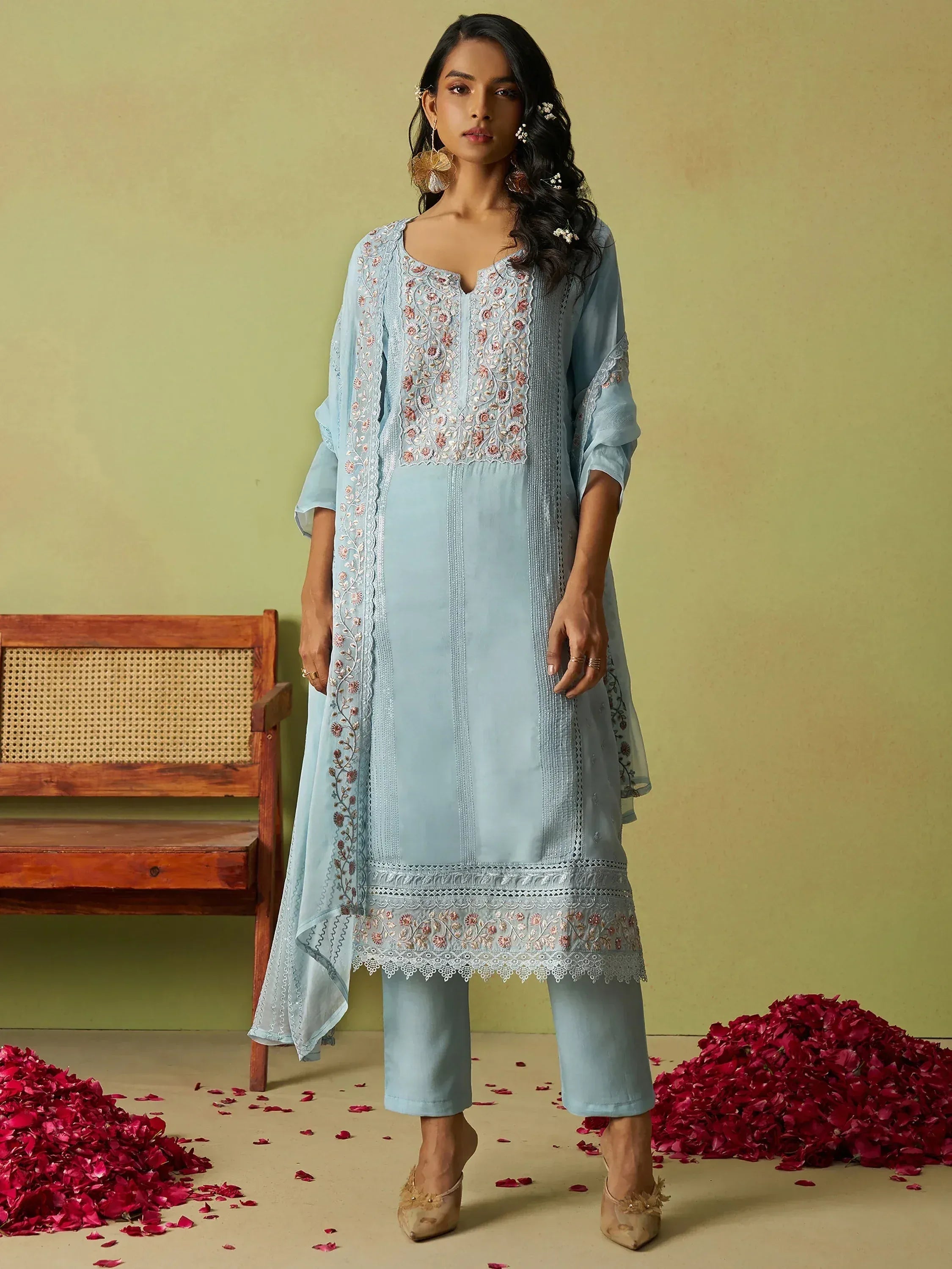 Light blue embroidered salwar kameez with floral detailing, paired with matching pants and dupatta, styled with rose petals.