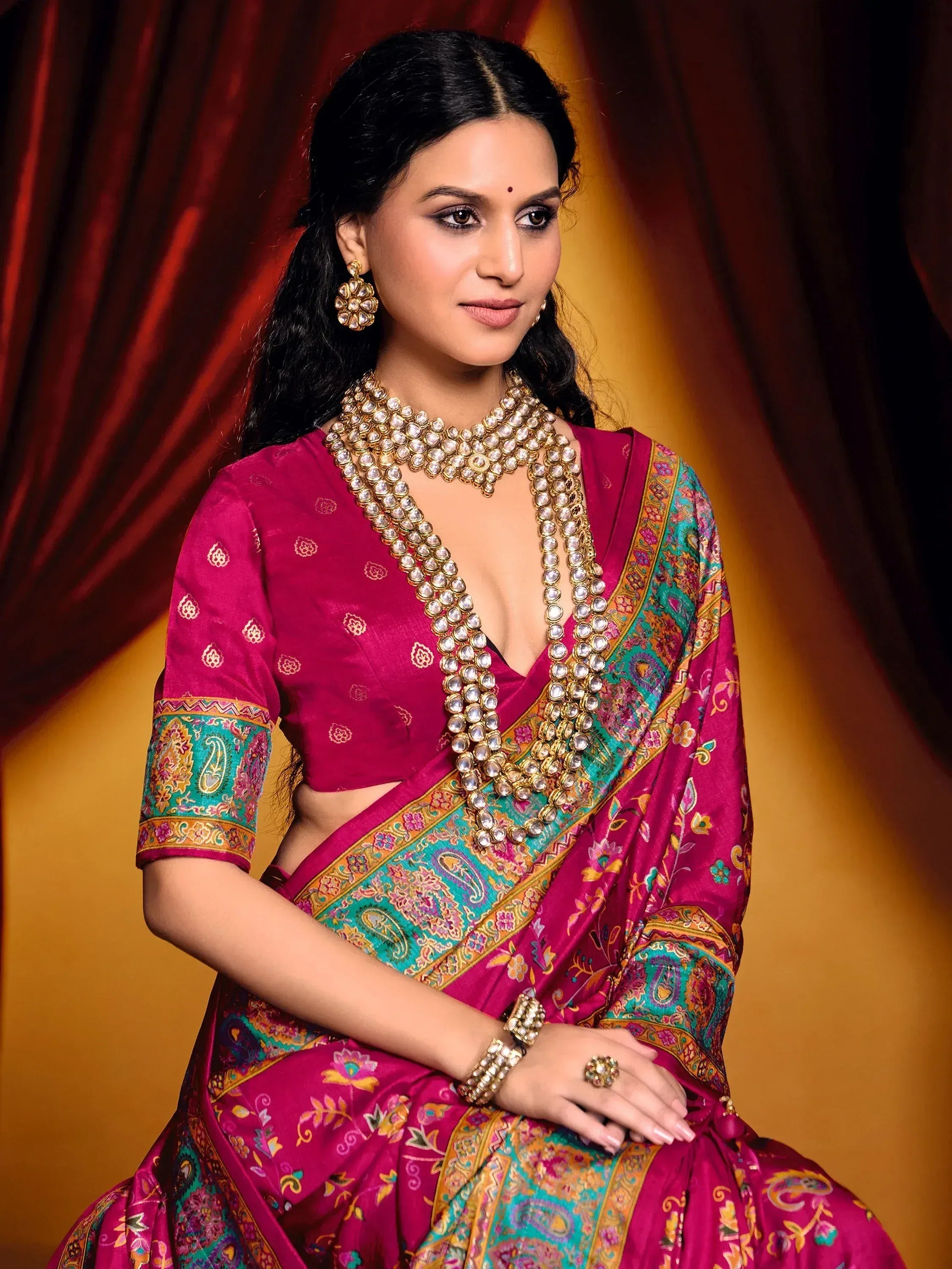 Woman in magenta Indian saree with gold jewelry, floral paisley border, and traditional ethnic wear styling