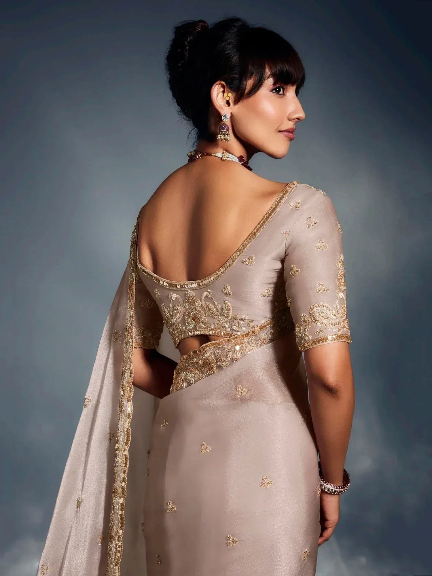 Elegant beige saree with gold embroidery, backless blouse, and traditional jewelry for Indian ethnic wear