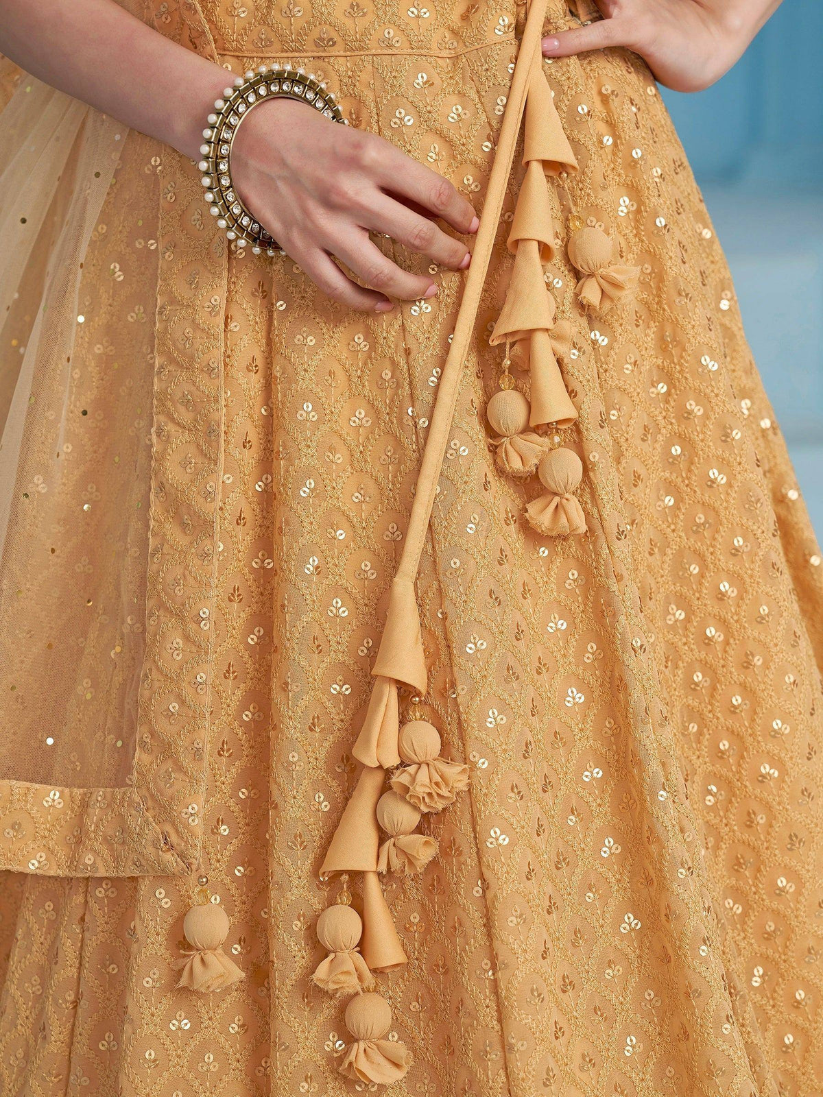 Mustard yellow lehenga with sequin embroidery and tassel details, paired with pearl bangle
