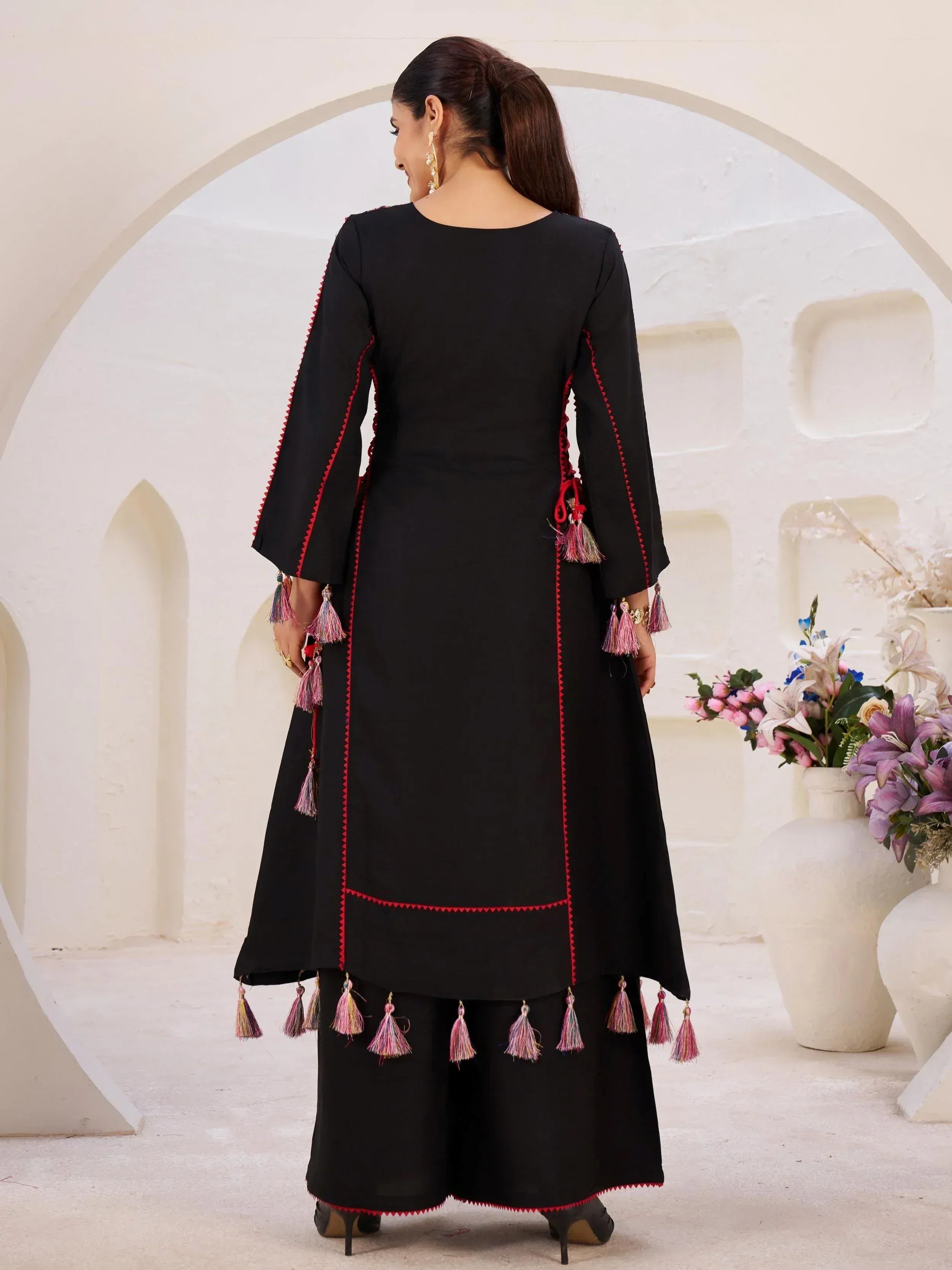 Black ethnic kurta with red trim and colorful tassels, paired with palazzo pants for festive occasions