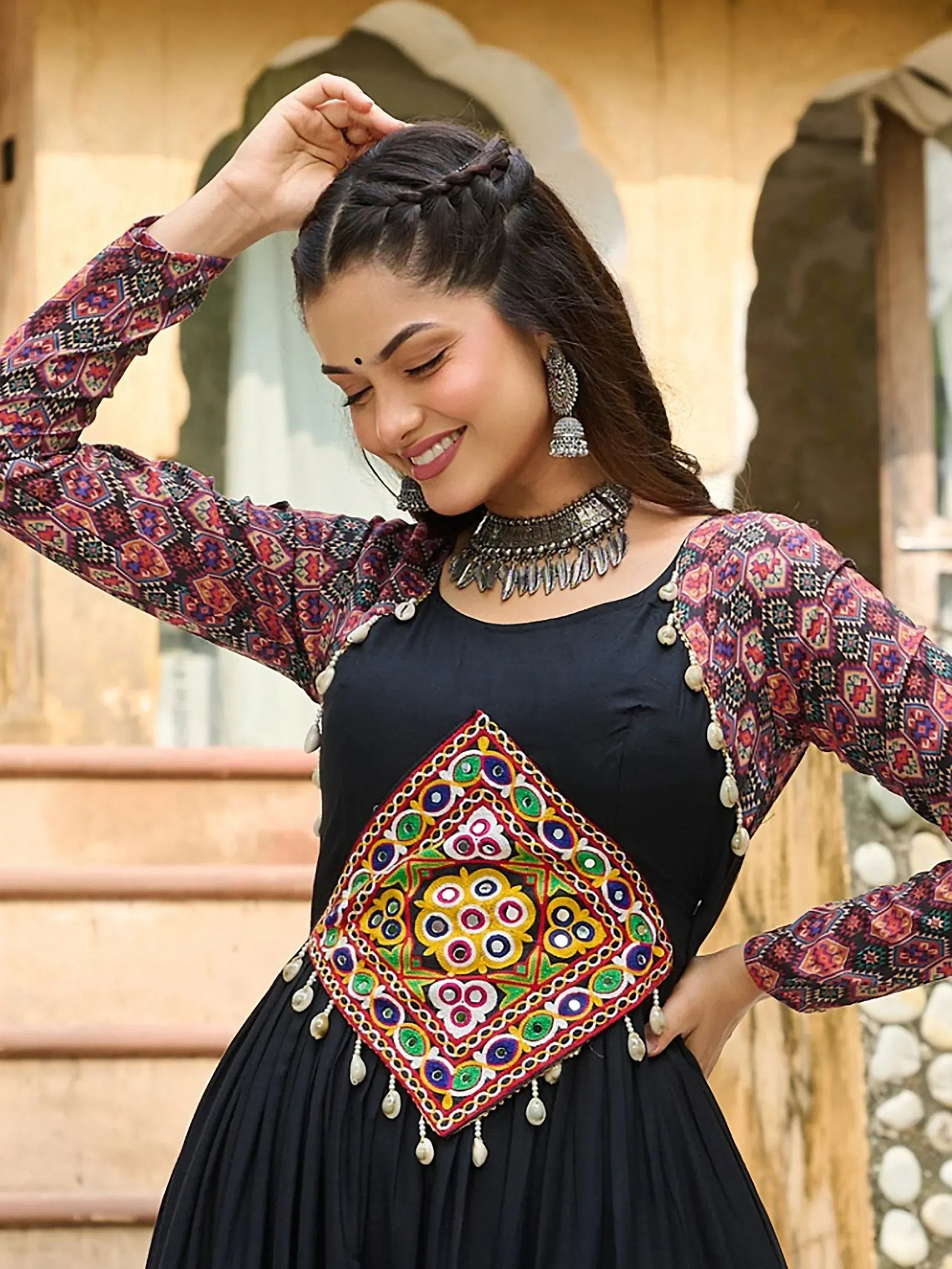 Woman in black ethnic gown with colorful mirror work and printed sleeves, styled with traditional jewelry