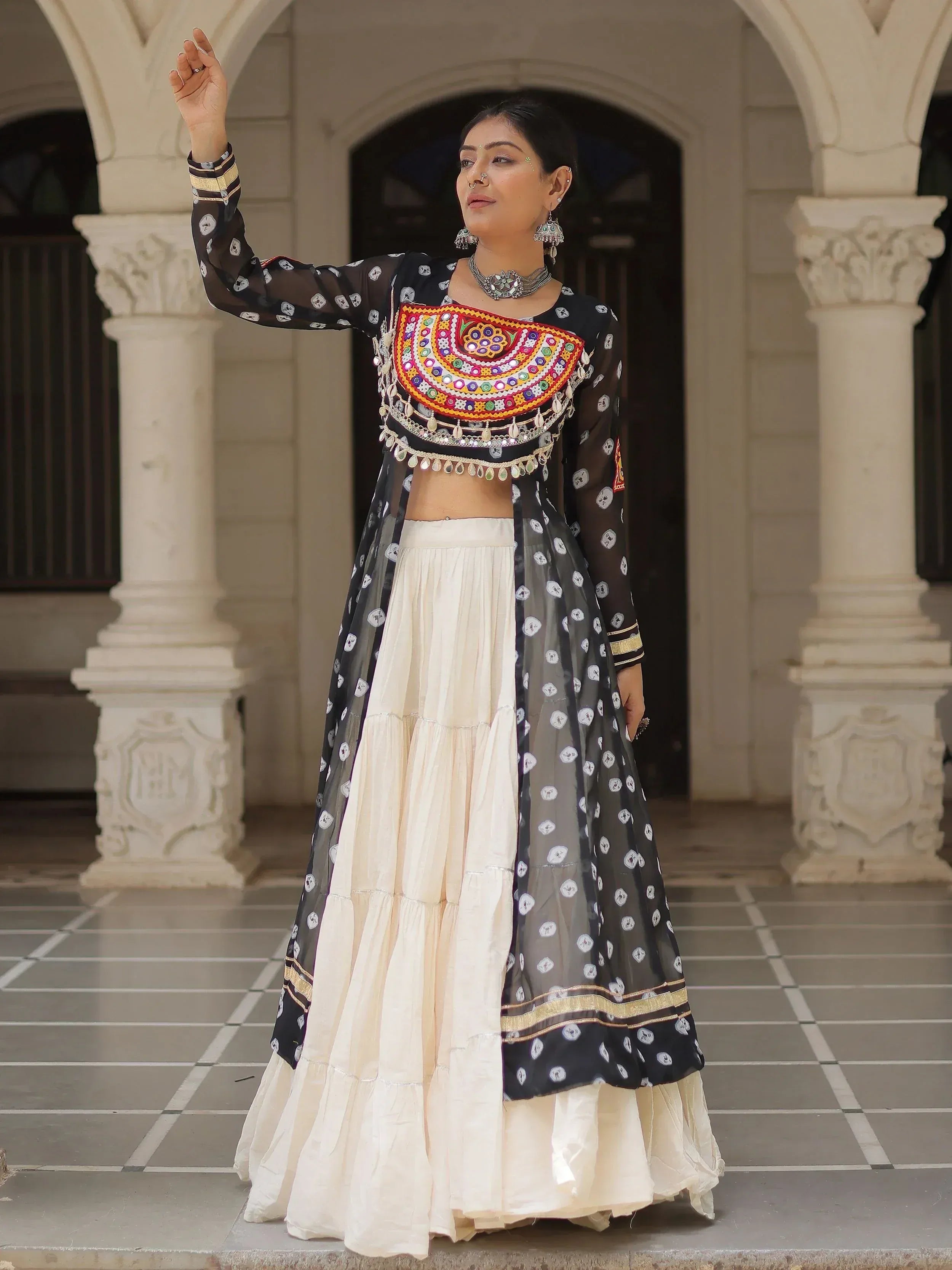 Woman in black and cream ethnic lehenga choli with mirror work, standing under arched doorway