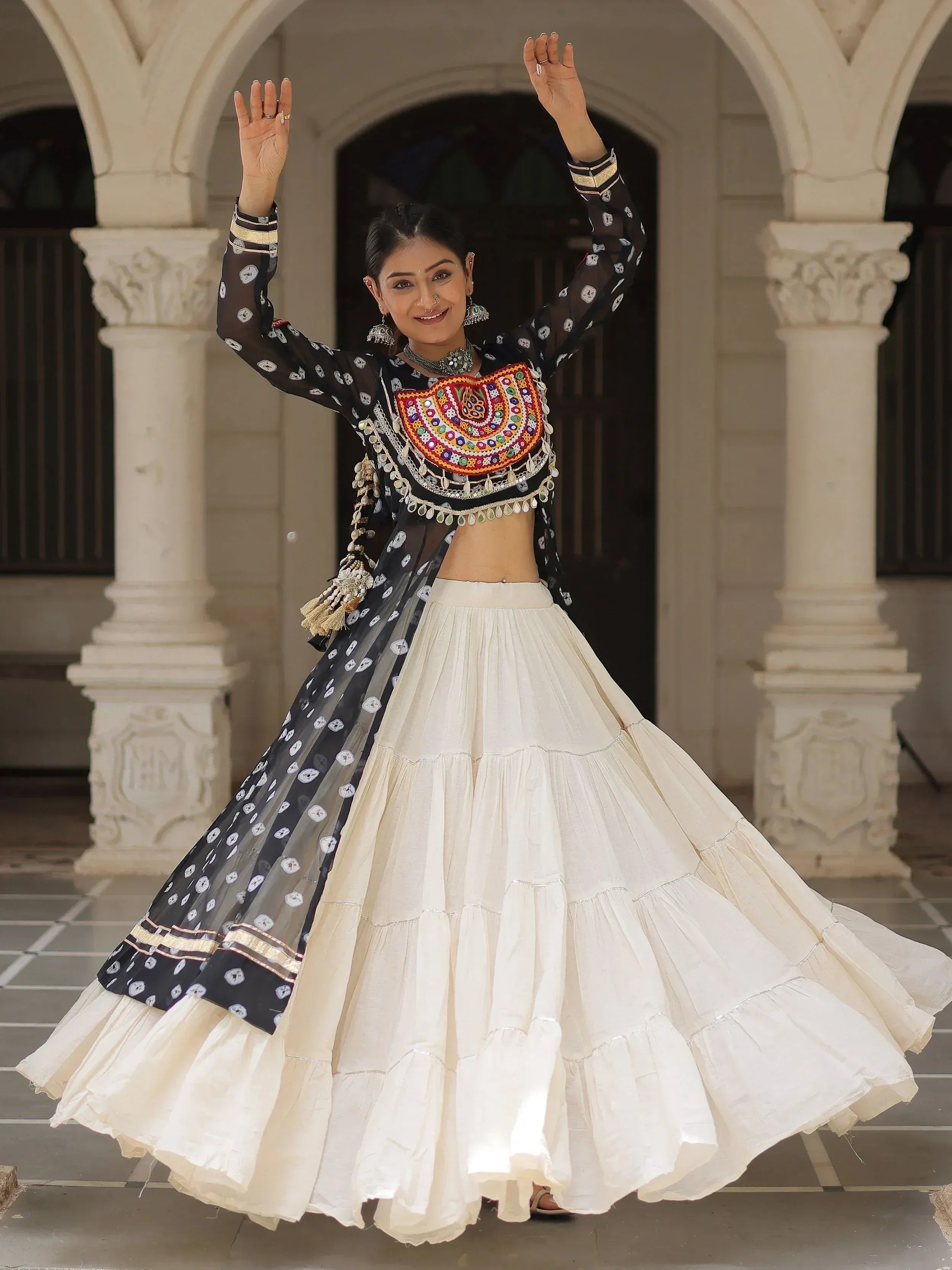 Woman in black and white ethnic lehenga choli with mirror work, dancing under arched doorway