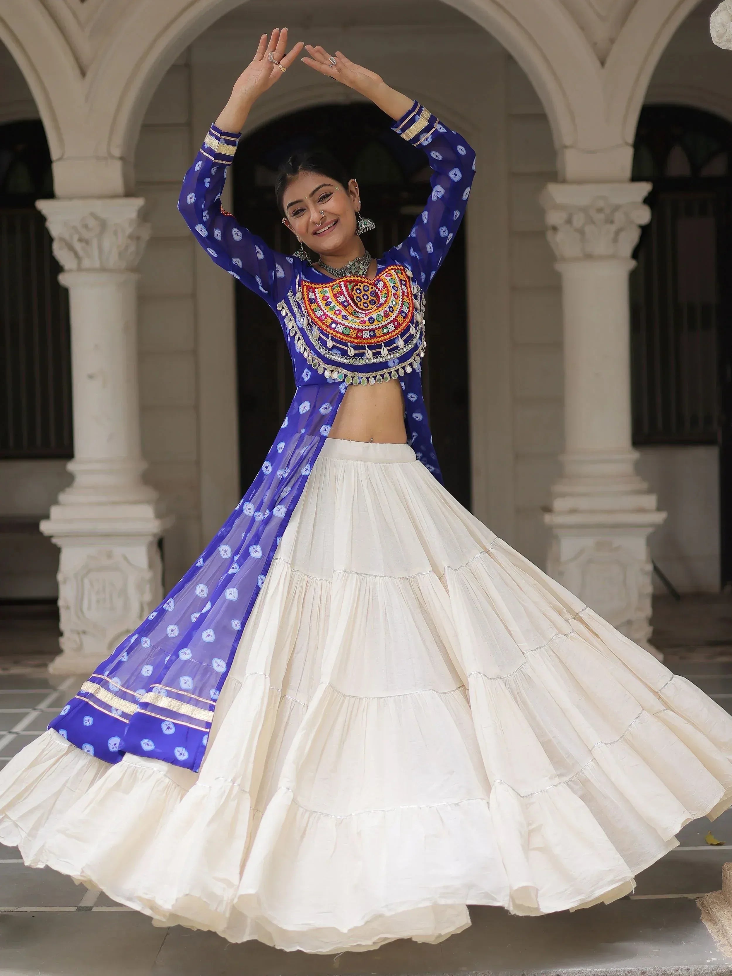 Woman in blue embroidered choli and white lehenga dancing under arches