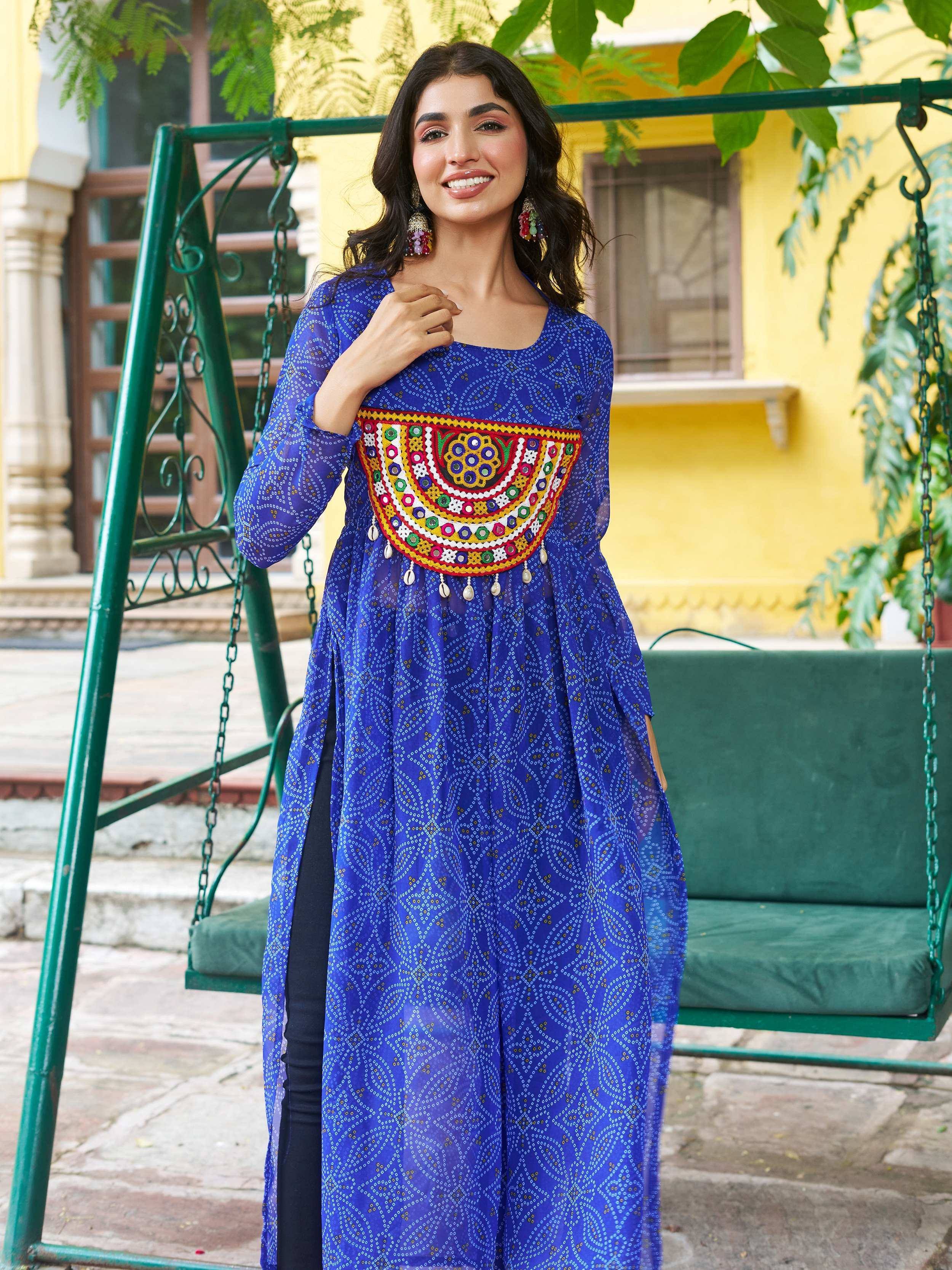 Blue printed ethnic kurti with colorful mirror work, worn with black pants near green swing