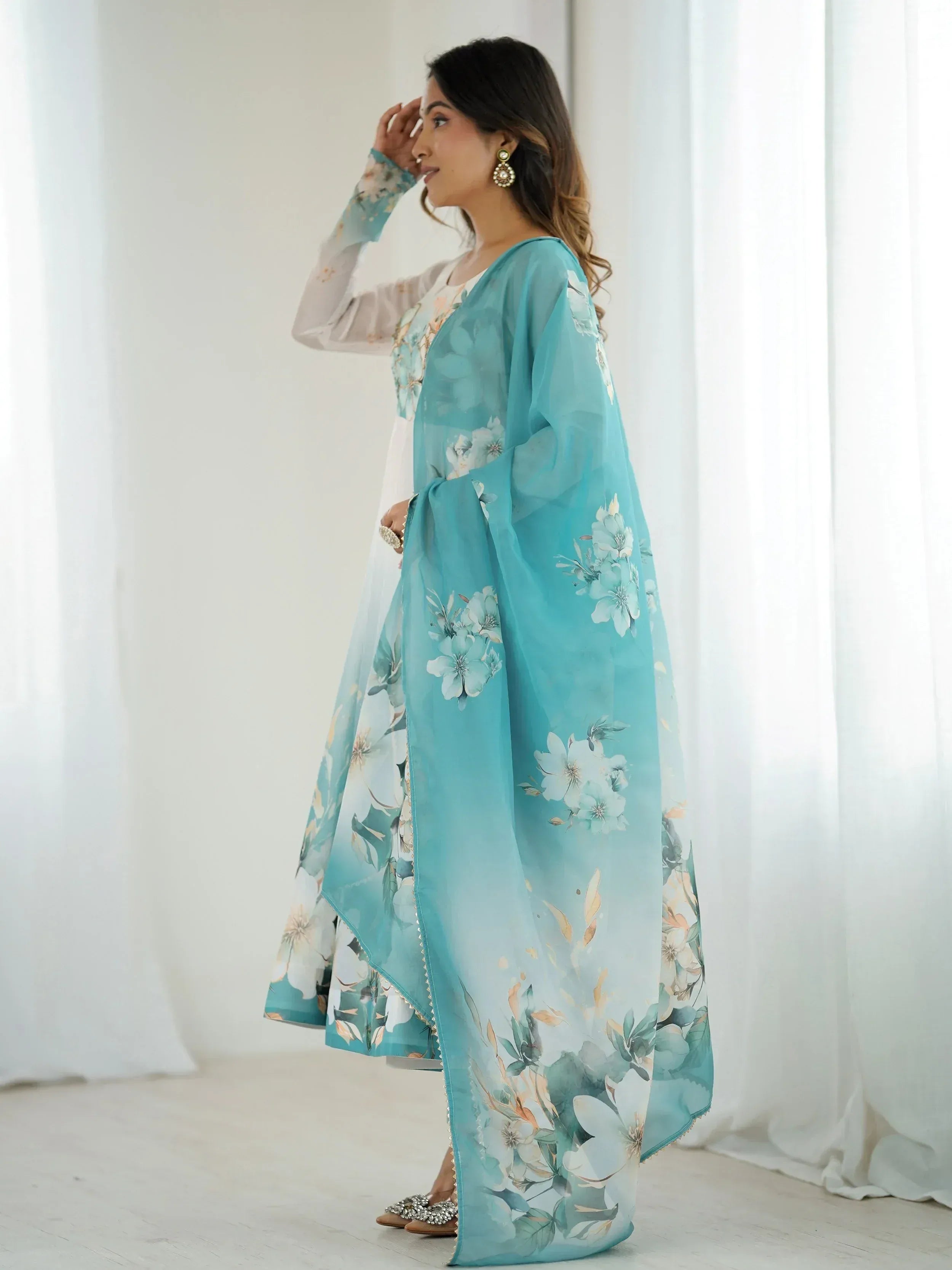 Woman in elegant turquoise floral print Indian ethnic gown with sheer dupatta, perfect for festive occasions.