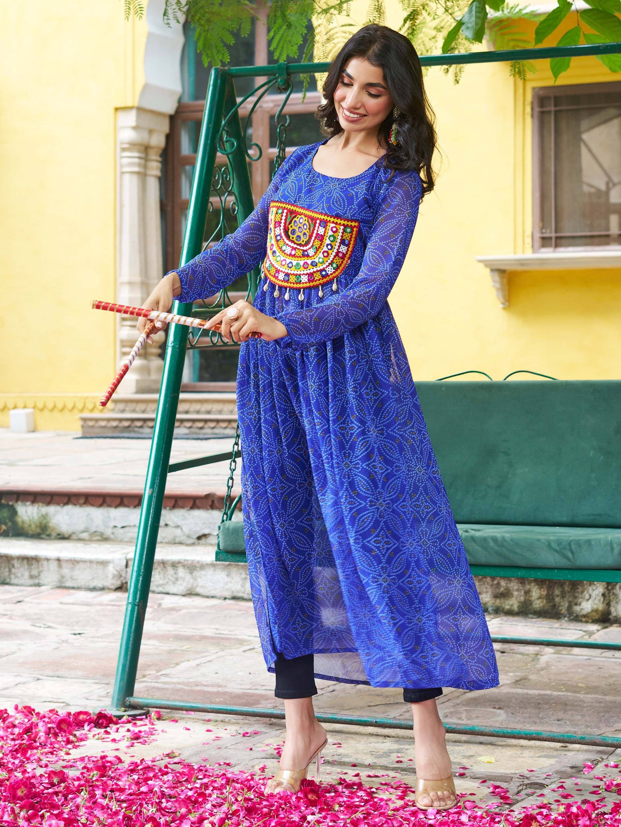 Woman in blue embroidered ethnic kurta with mirror work, standing by swing amidst rose petals