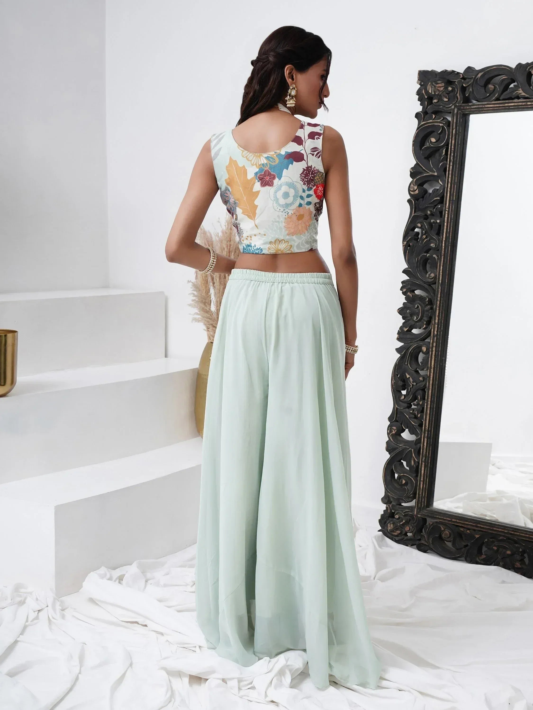 Woman in pastel palazzo pants and floral sleeveless blouse, wearing ethnic jewelry